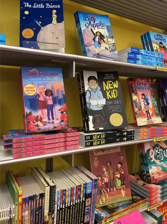 Books on a yellow shelf, including children's stories and novels, with colorful covers and titles visible.