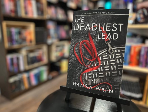 Book titled 'The Deadliest Lead' by Hanna Wren displayed on a stand in a bookstore, with shelves of books in the background.