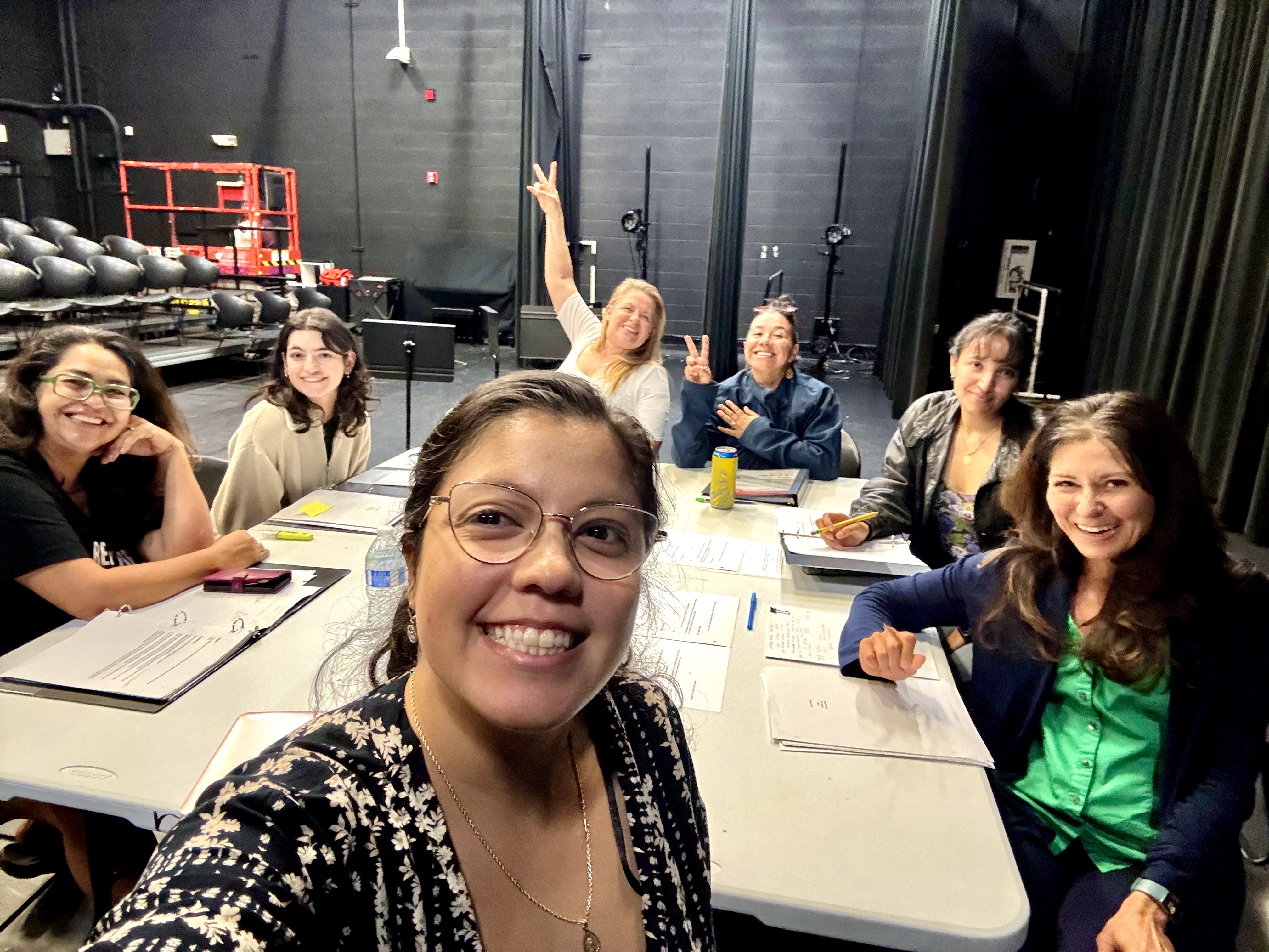 Group of seven women sitting around a table in a studio, smiling and looking at the camera.