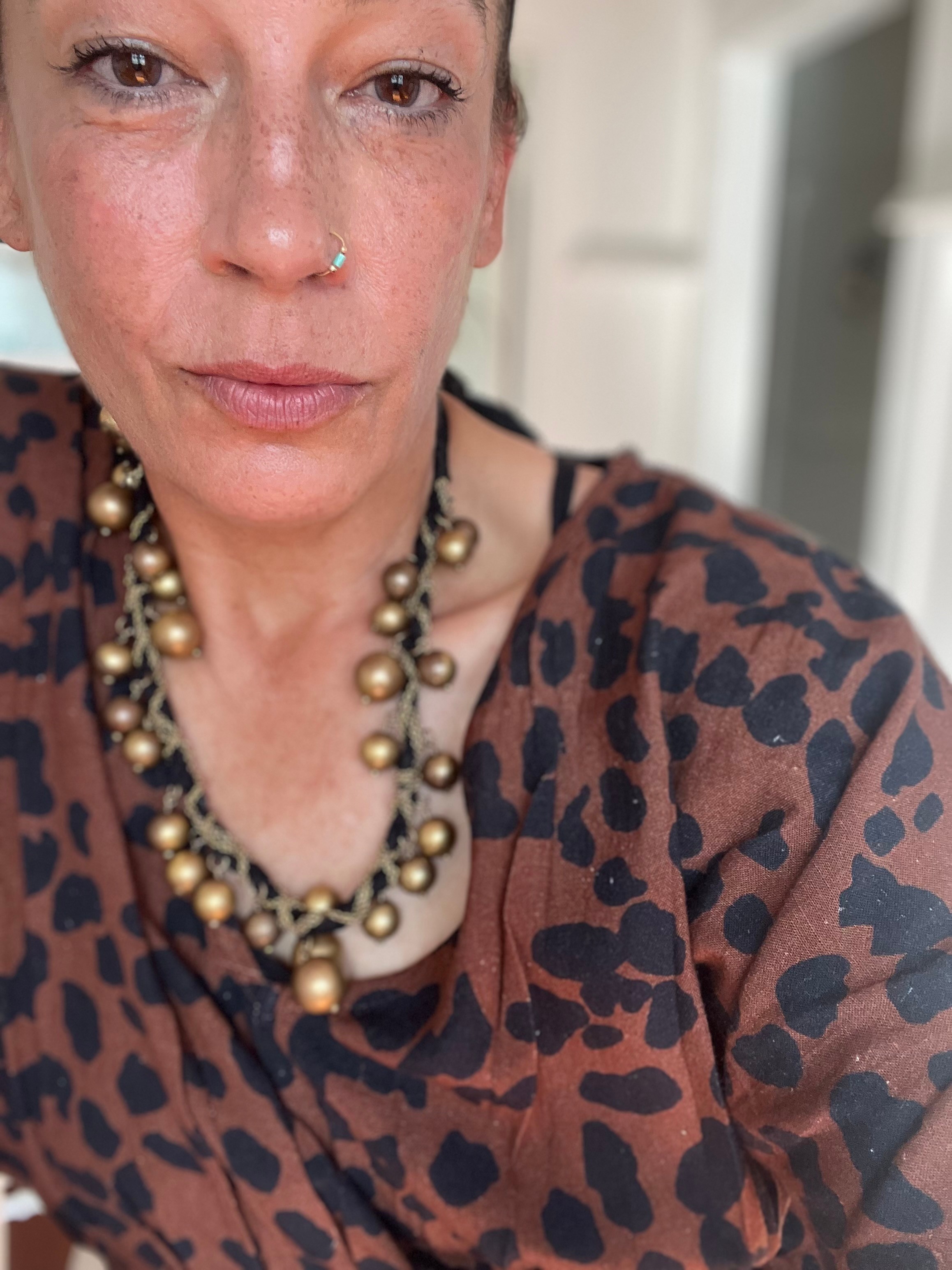 Close-up of a woman wearing a leopard print top and a gold and black beaded necklace, with a neutral background.