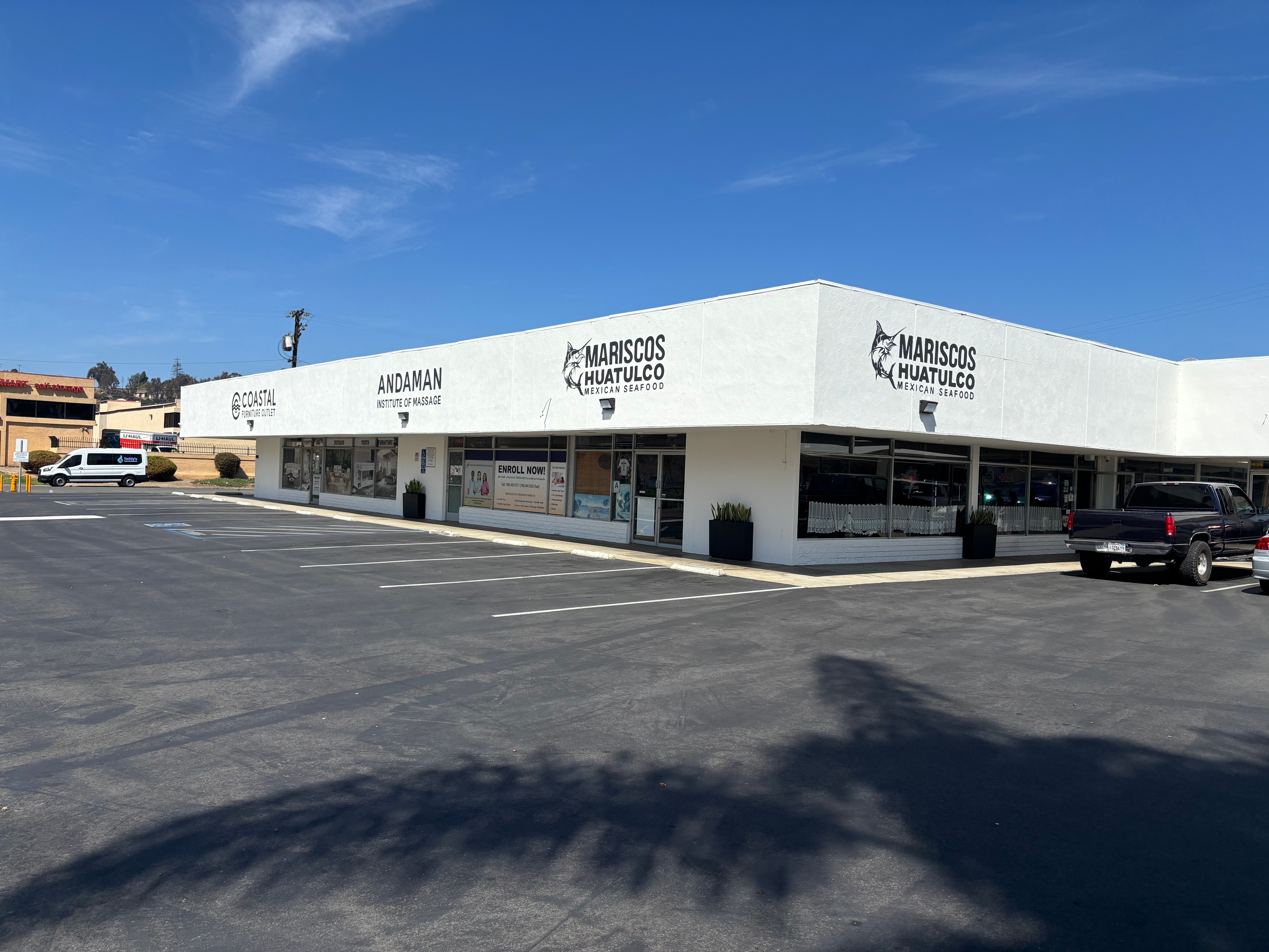Single-story building with signs for seafood stores, parking lot in front, under a blue sky with some clouds.