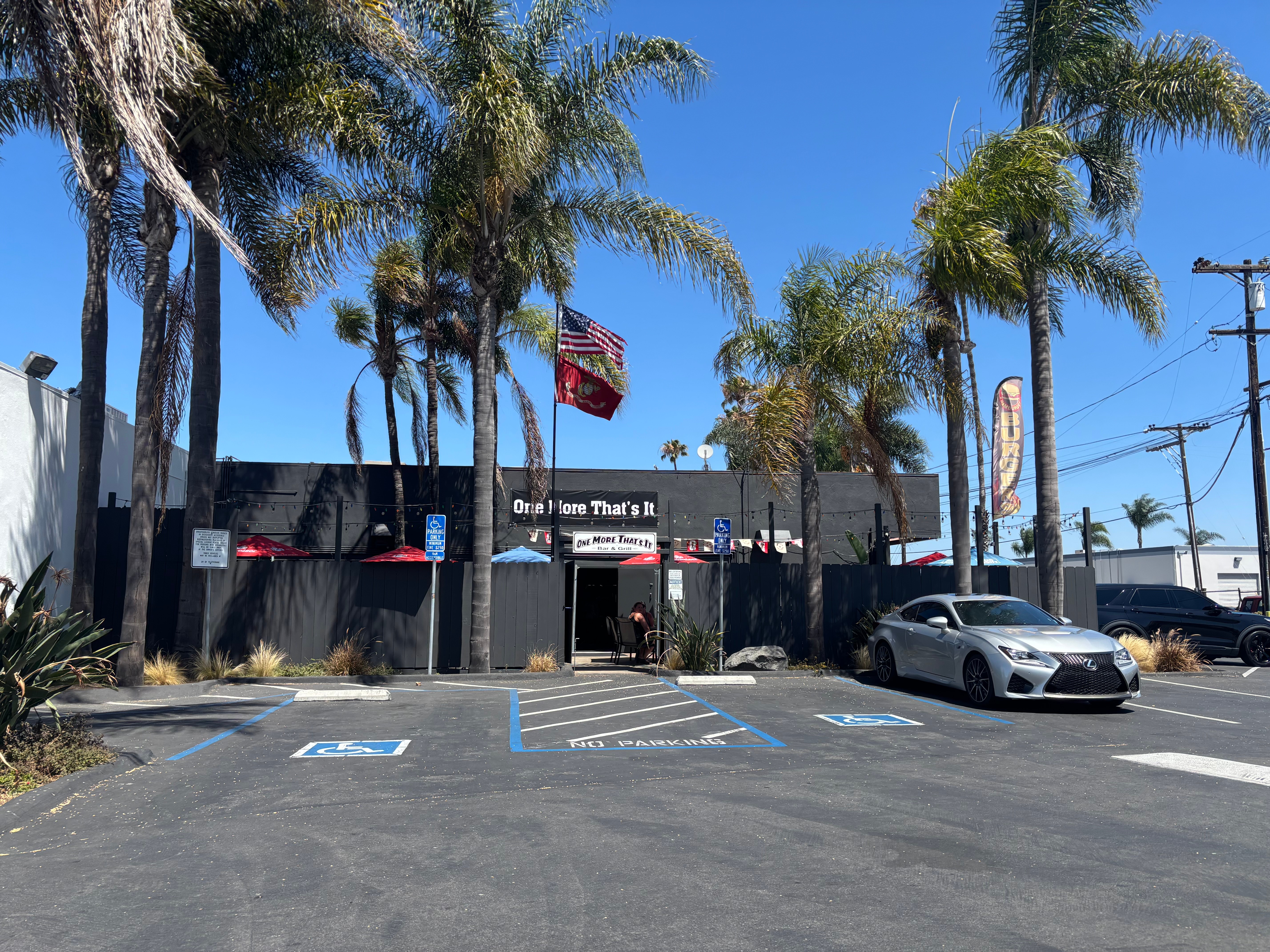 Parking lot with a building, palm trees, and a white car parked, under a clear blue sky.