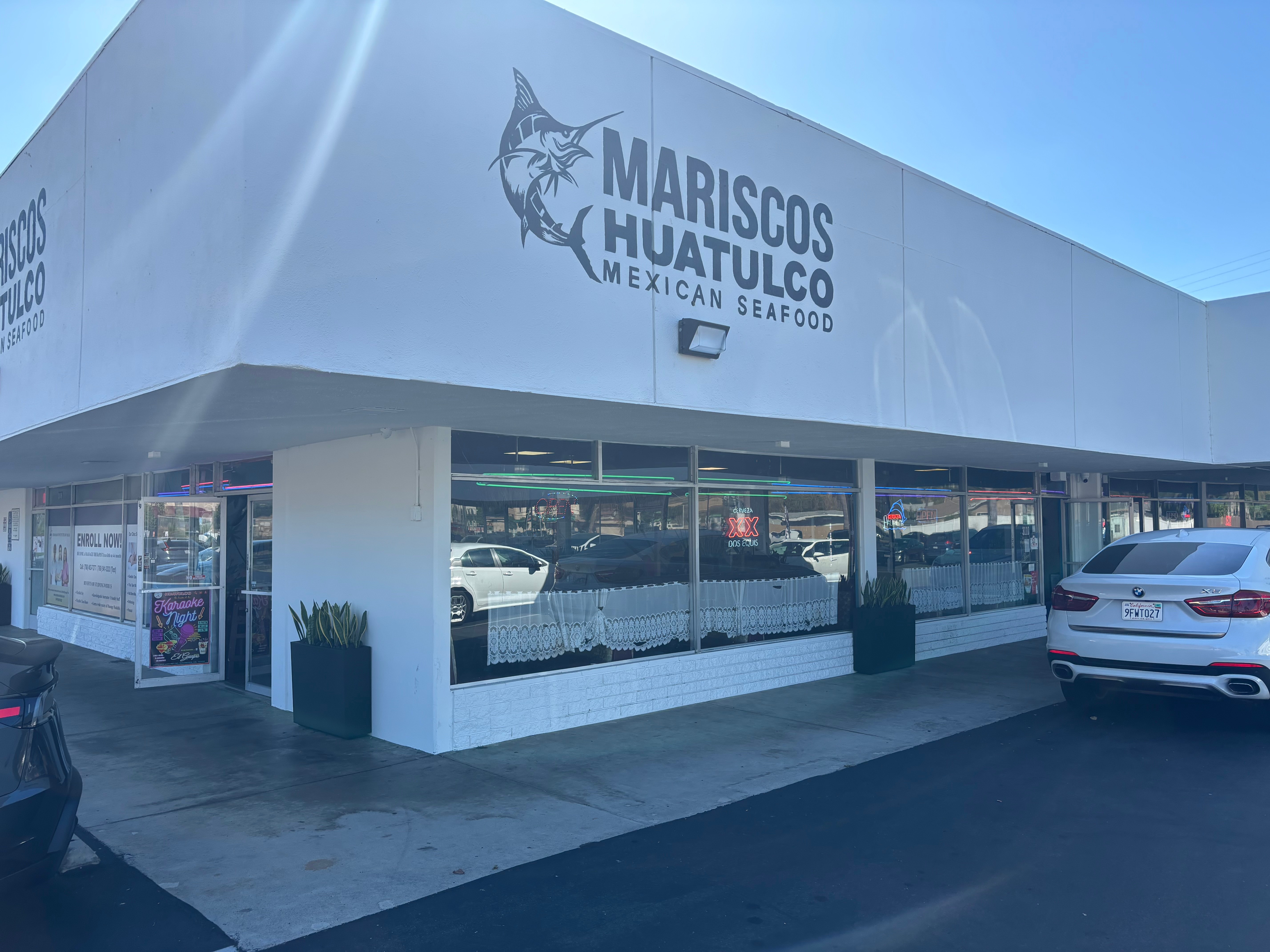 Mariscos Huatulco Mexican seafood restaurant with large sign and glass windows, parked cars outside, sunny day.