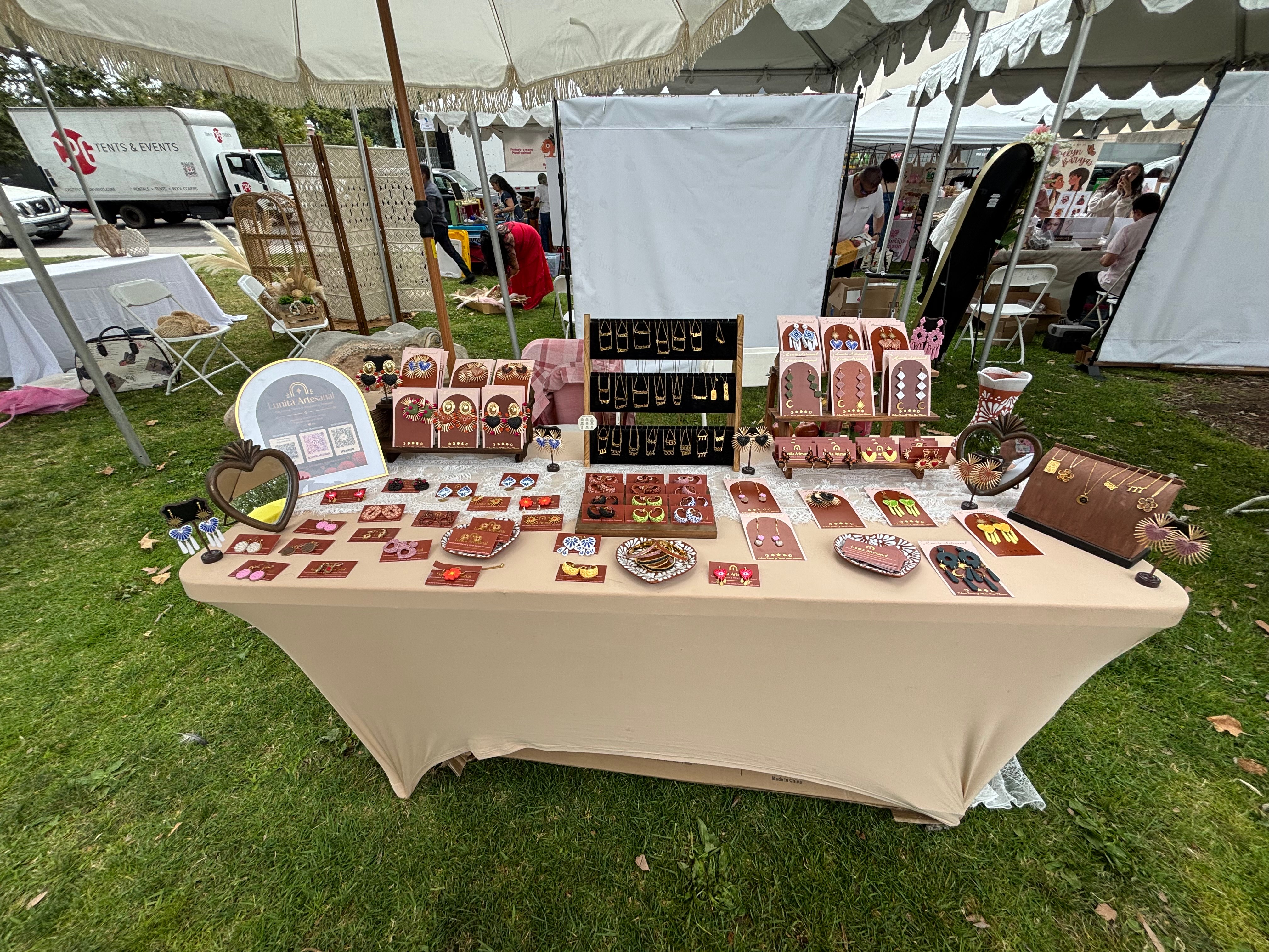 Table with jewelry and accessories displayed outdoors under a tent, with people and tents in the background.