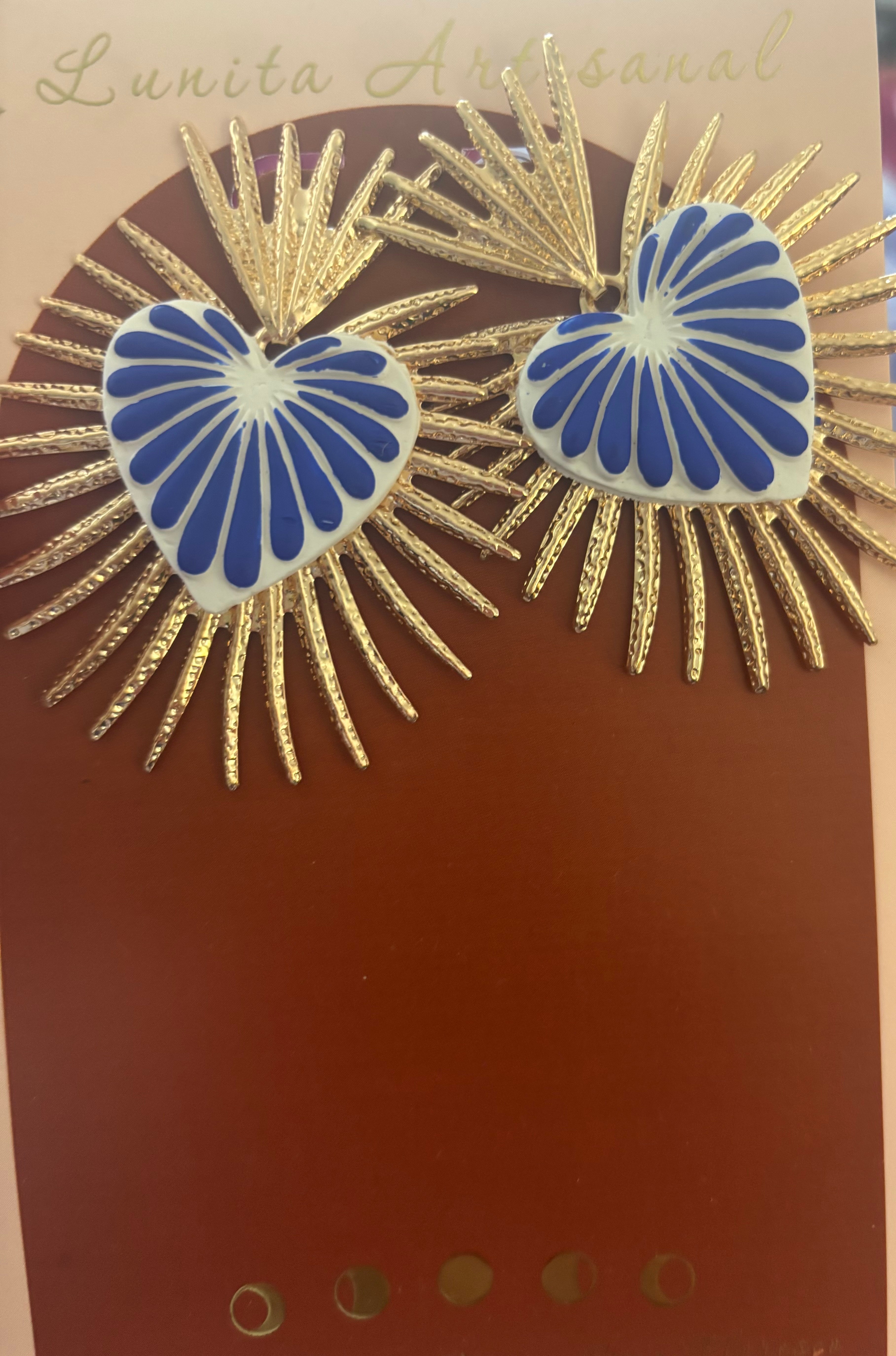 Pair of earrings with blue and white heart-shaped centers and gold spiky radiating designs, on a brown background.