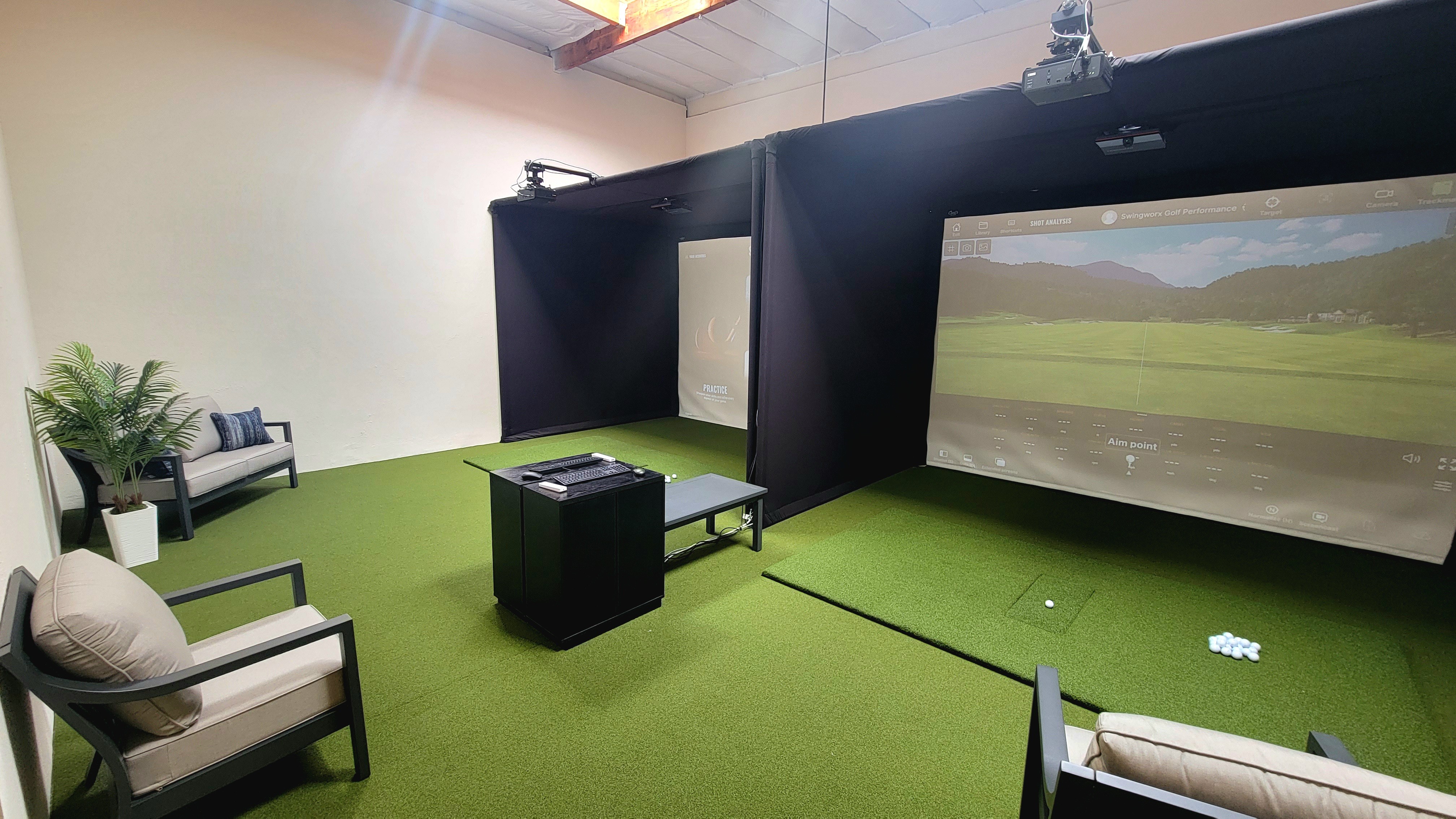 Indoor golf simulation room with chairs, a screen, and artificial grass flooring.