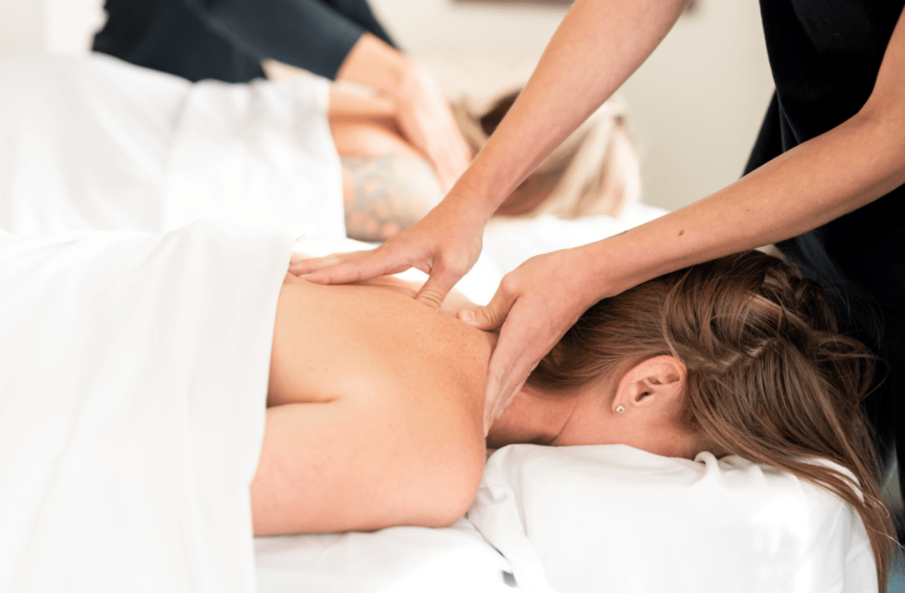 Person receiving a massage on their back while lying face down on a massage table, with another person applying pressure.