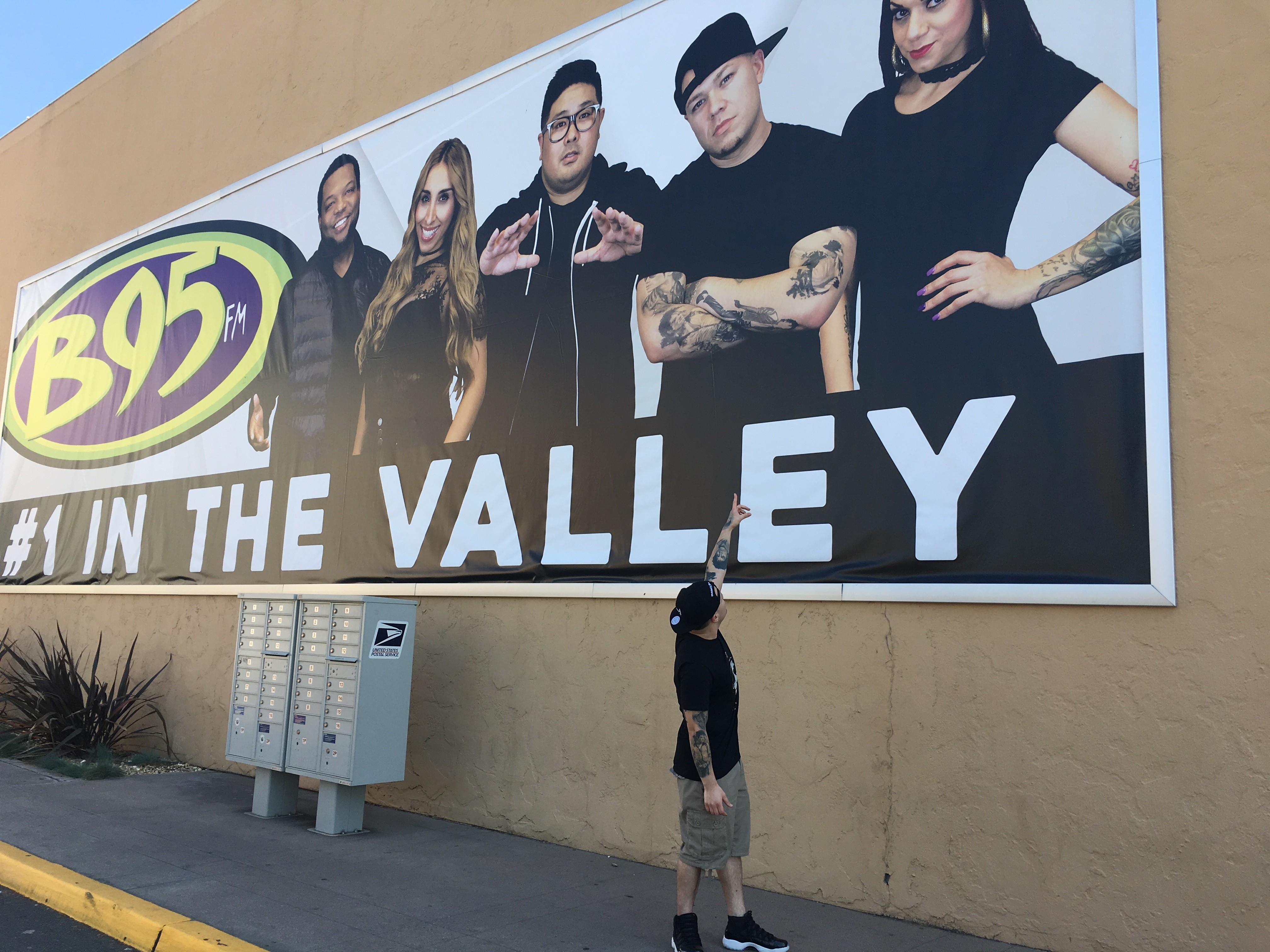 Person standing in front of a large billboard featuring six people, with a logo and text, on a beige wall.