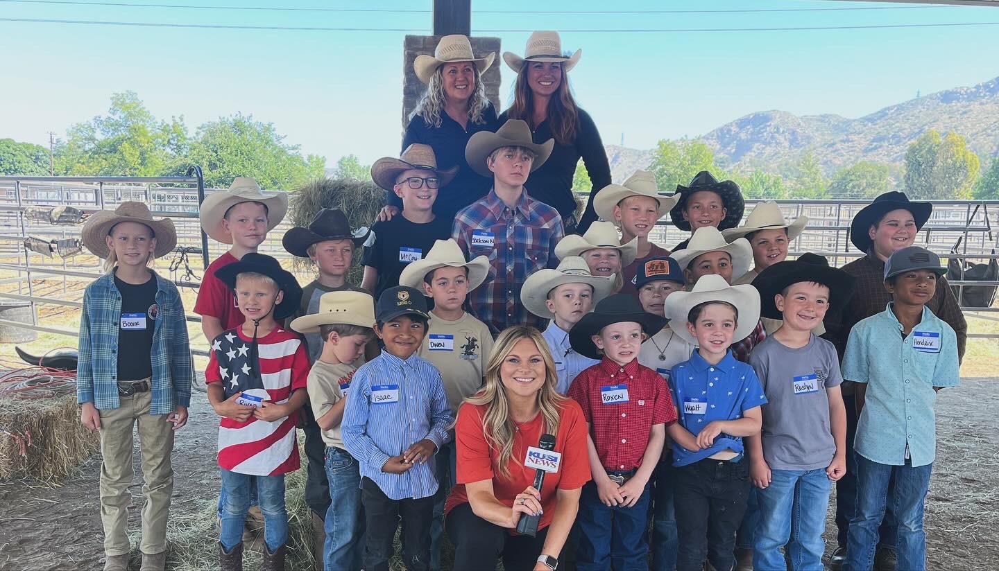 Group of children and two adults outdoors, some wearing cowboy hats, with mountains in the background.