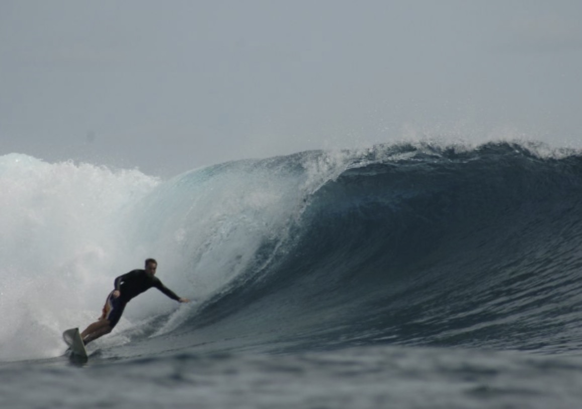 Surfer riding inside a large wave with white foam, ocean and cloudy sky in background.
