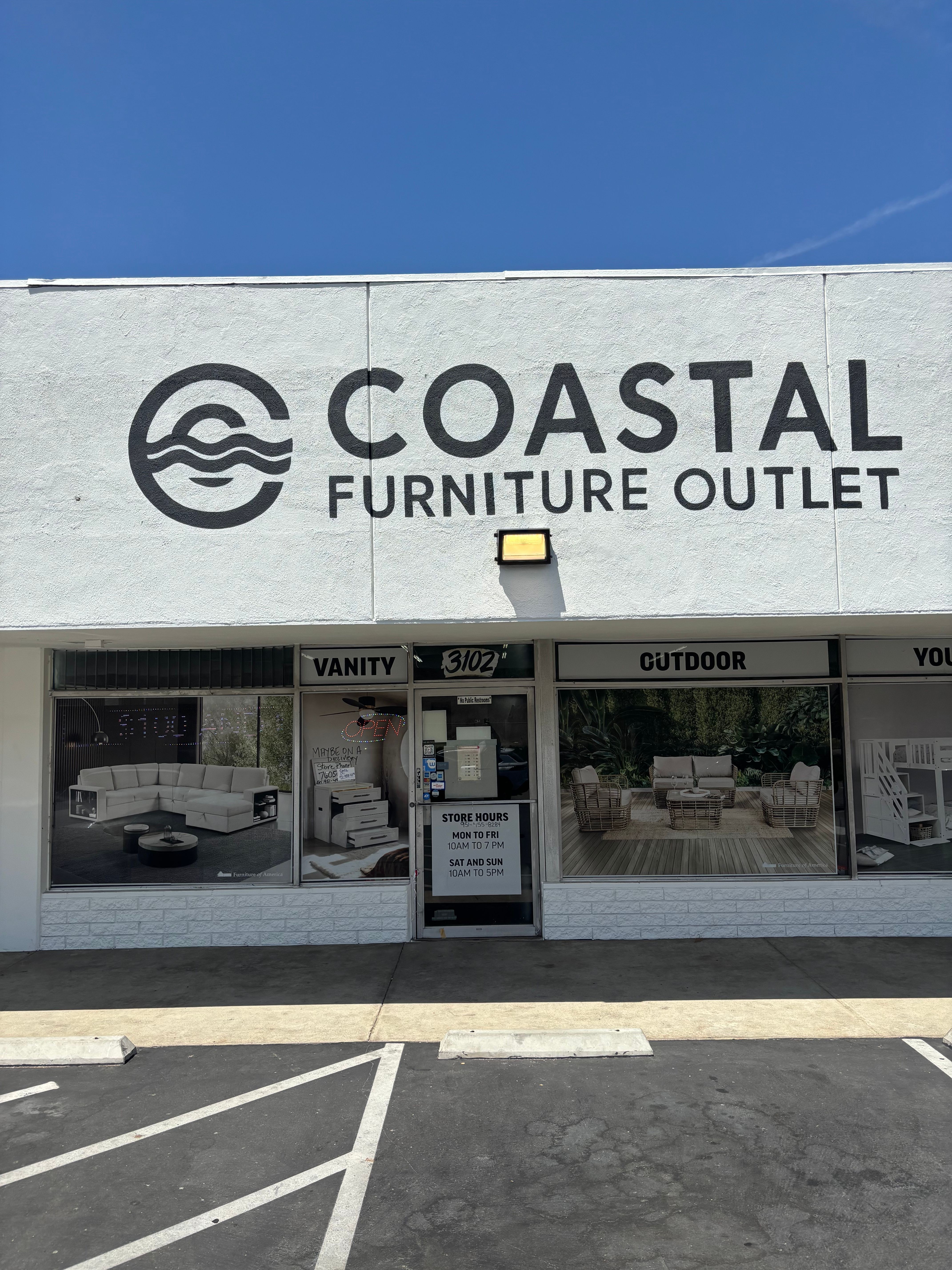 Storefront with large sign reading 'COASTAL FURNITURE OUTLET' and glass windows showing furniture inside.