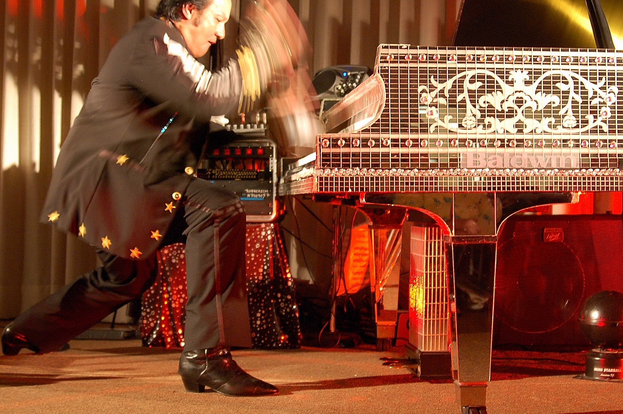 Performer playing a grand piano on stage with motion blur, stage lights, and curtains in background.