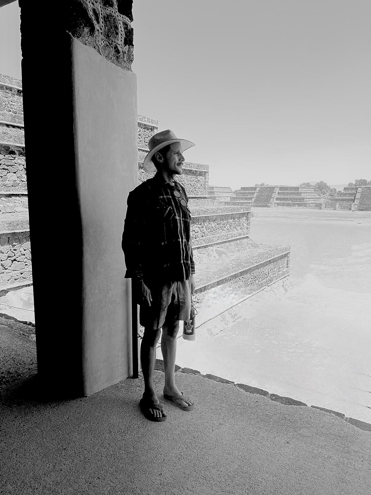 Person wearing a hat and dark clothing standing near a wall, overlooking a body of water or landscape.