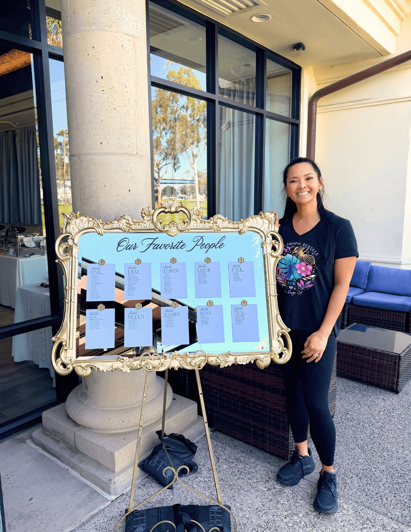 Woman standing next to a decorative framed board with papers, outside building with large windows and seating area.