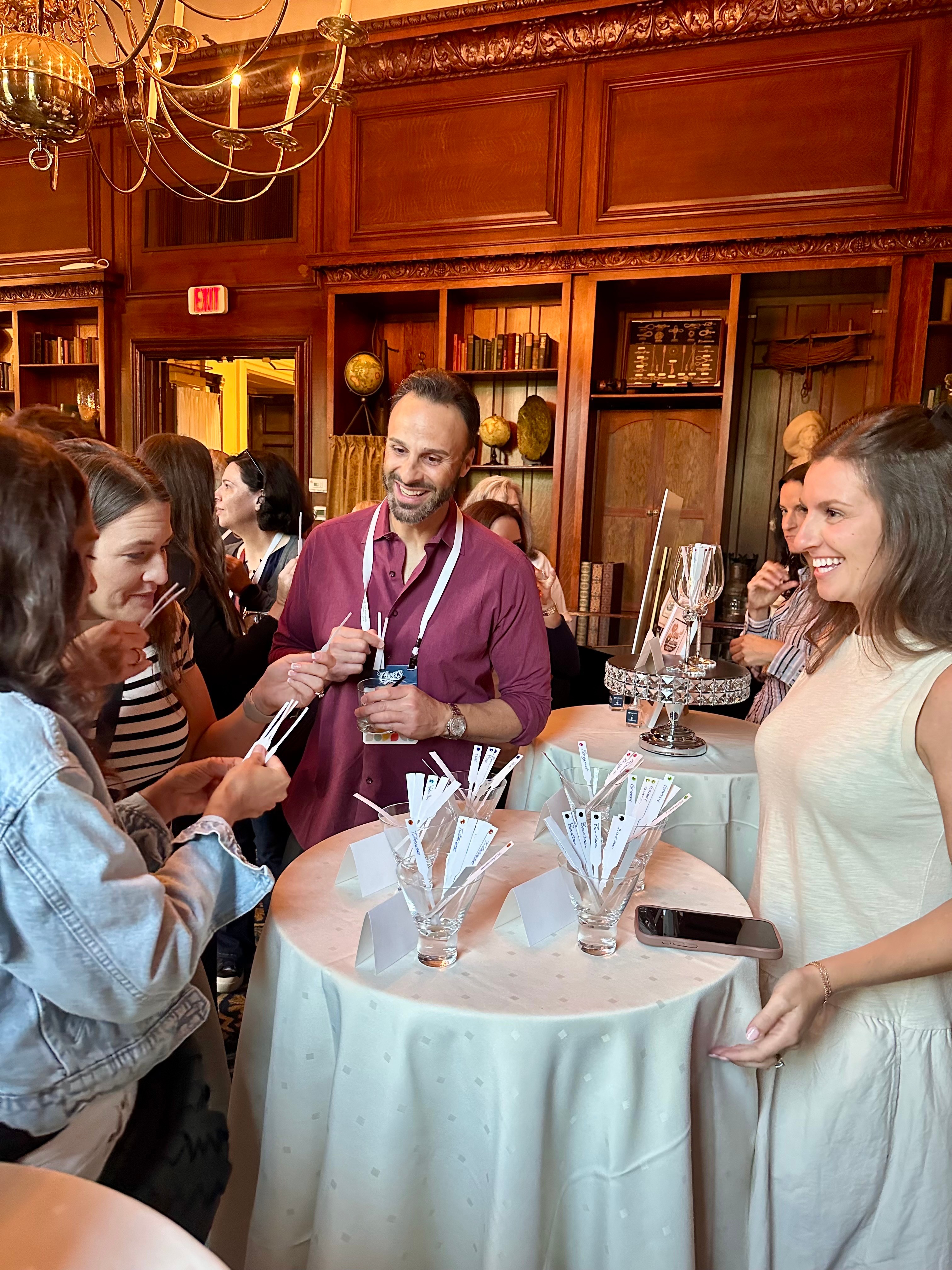 Group of people socializing around a table in a room with wooden shelves and a chandelier.