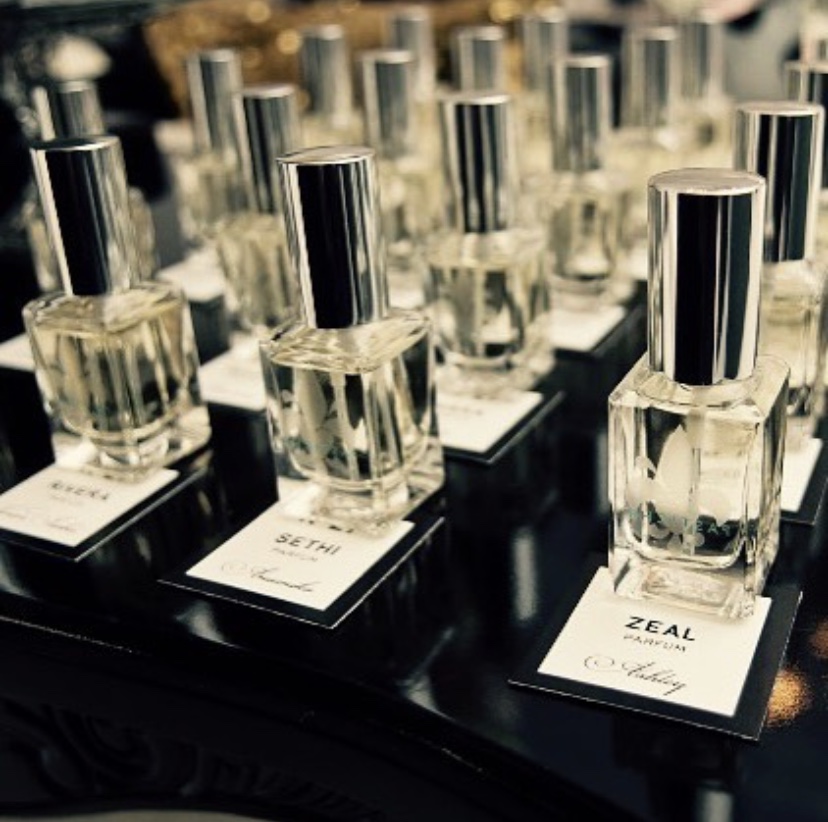 Multiple bottles of perfume with silver caps on display, each on a black stand with a white label, in a retail setting.