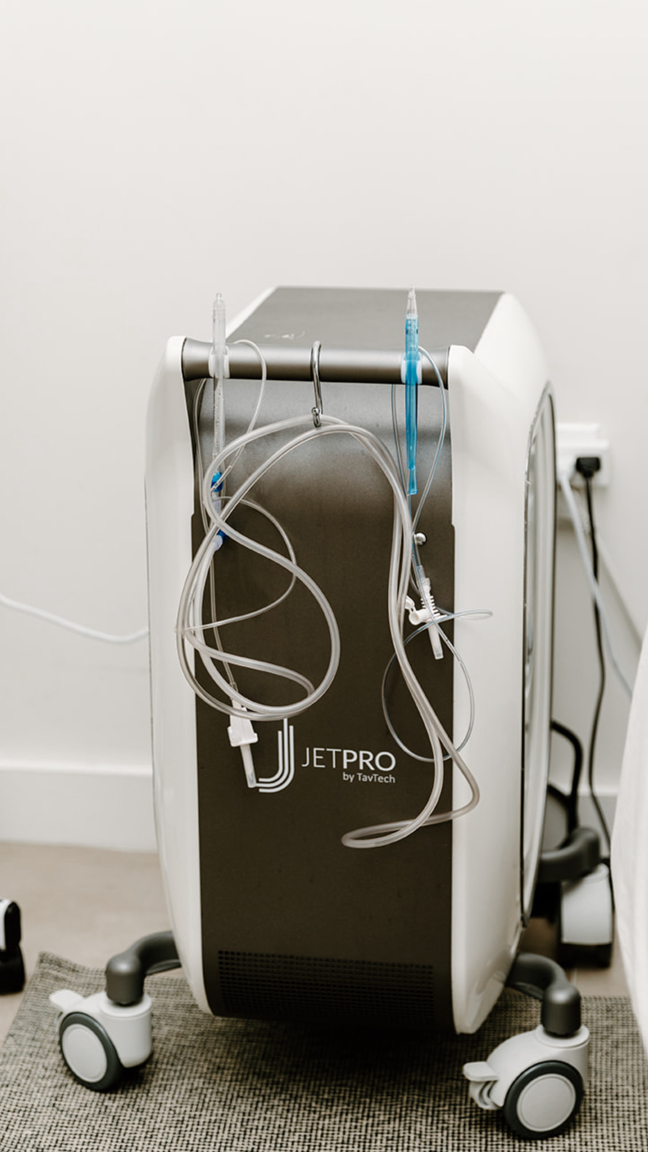 Medical device with tubes and wires on a wheeled stand, plugged into a wall socket, against a plain wall.