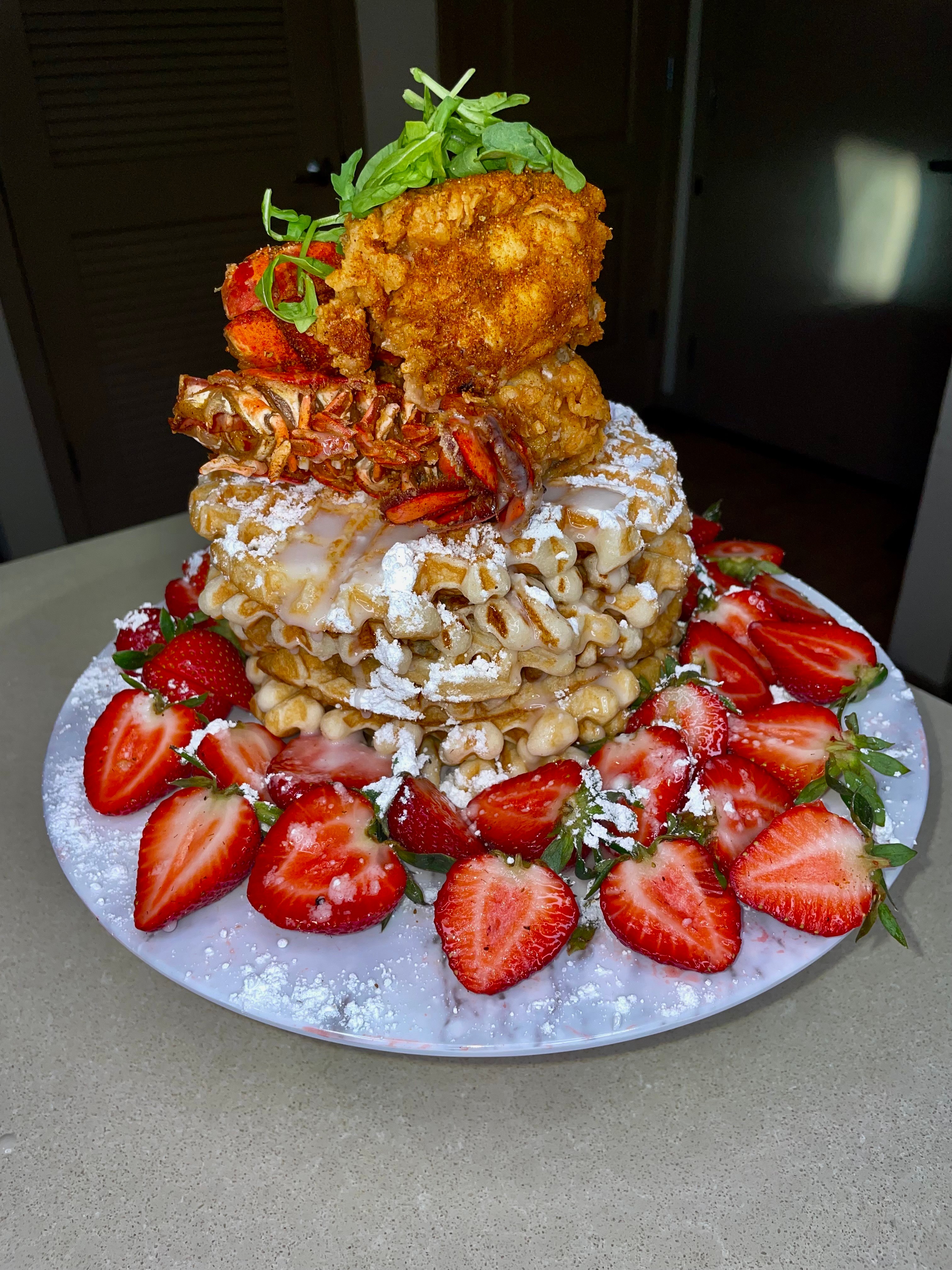 Stacked dessert with fried chicken, strawberries, whipped cream, and garnishes on a plate.