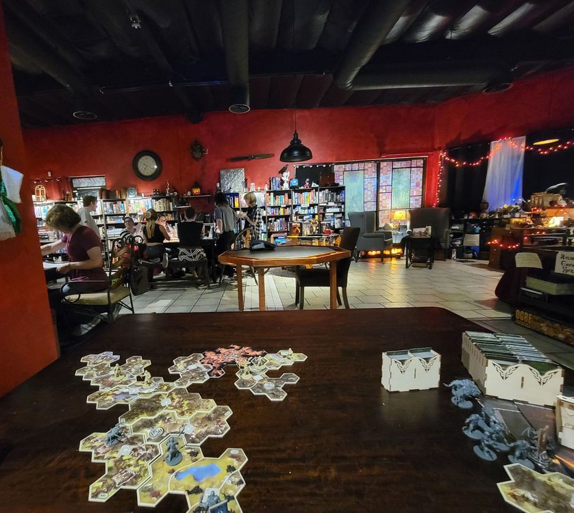 Board game pieces and cards on a table in a cozy, dimly lit room with red walls and shelves.