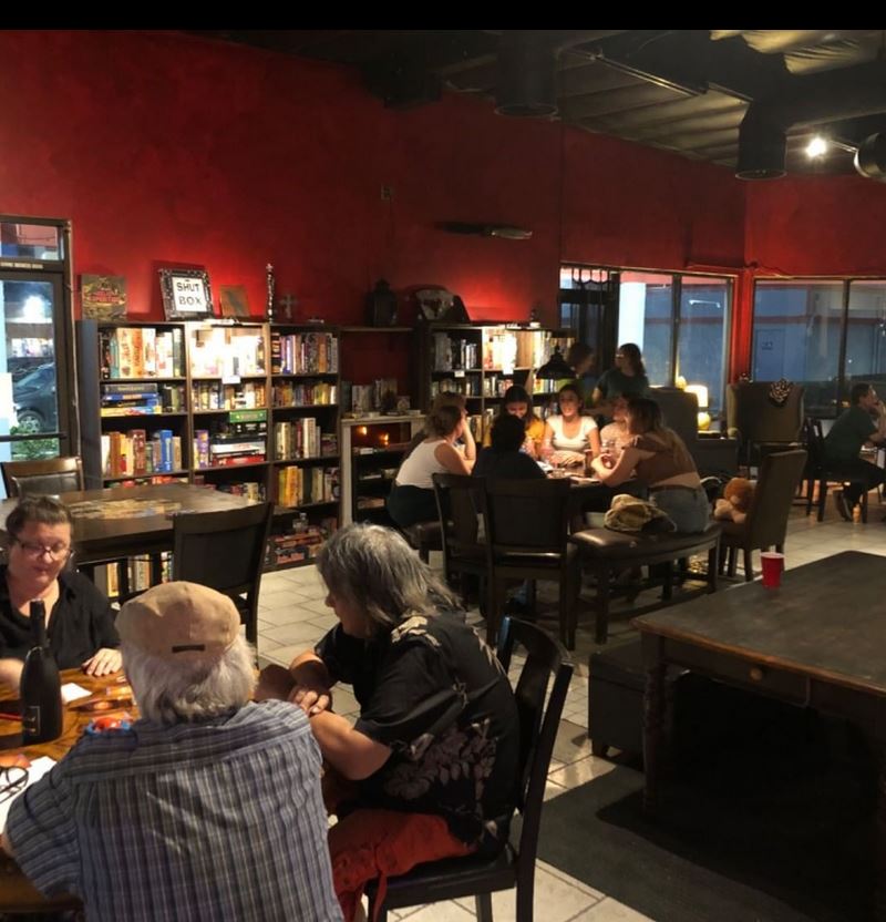 People sitting at tables in a cozy room with red walls and bookshelves, engaging in conversation and activities.