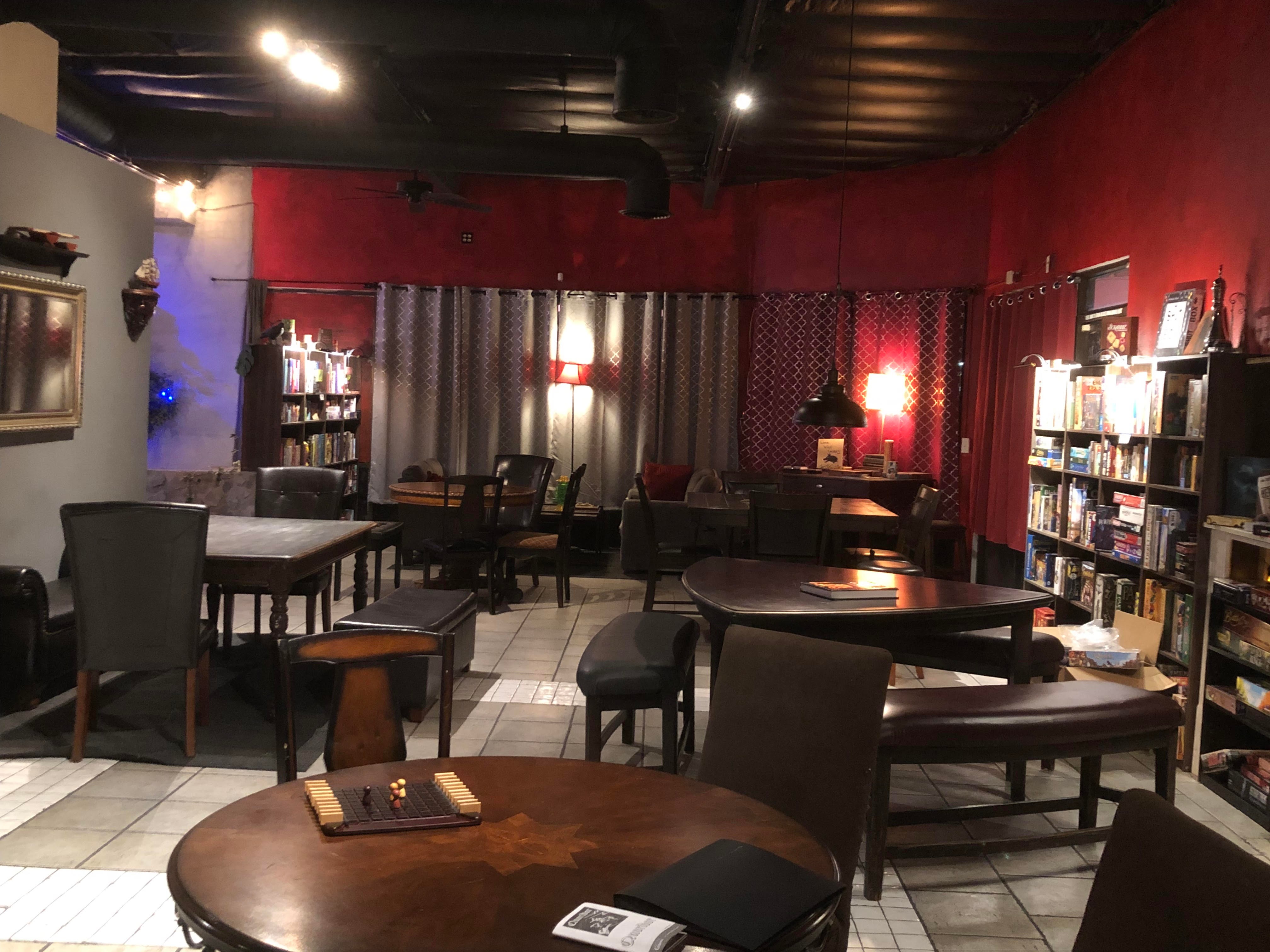 Room with tables, chairs, bookshelves, and curtains, red and black walls, and warm lighting.