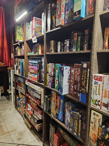 Bookshelves filled with colorful board games and books in a store, with a red curtain in the background.