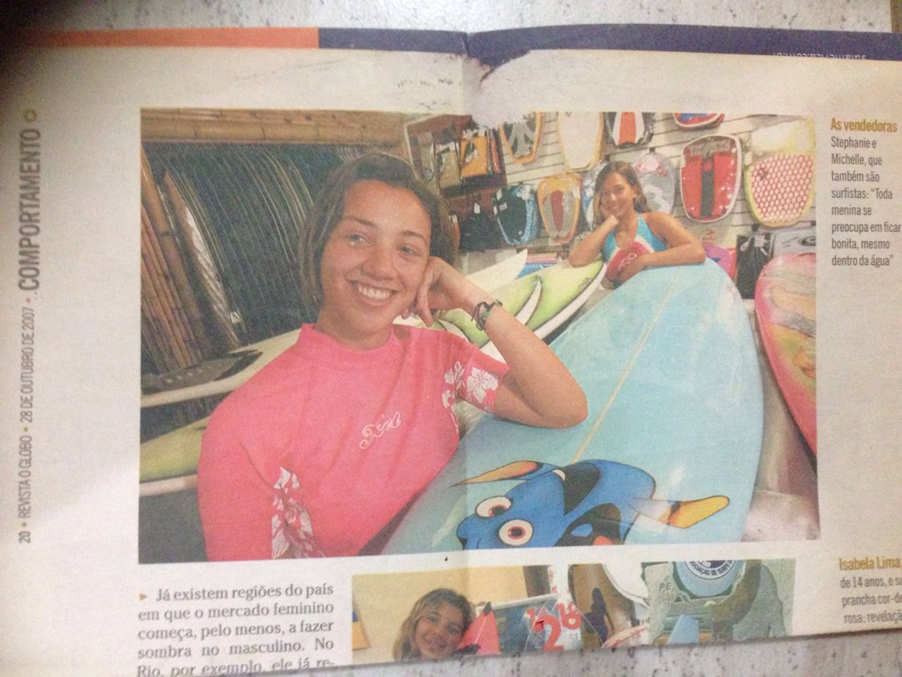 Two smiling girls sitting at a table with colorful bags and shelves in the background.