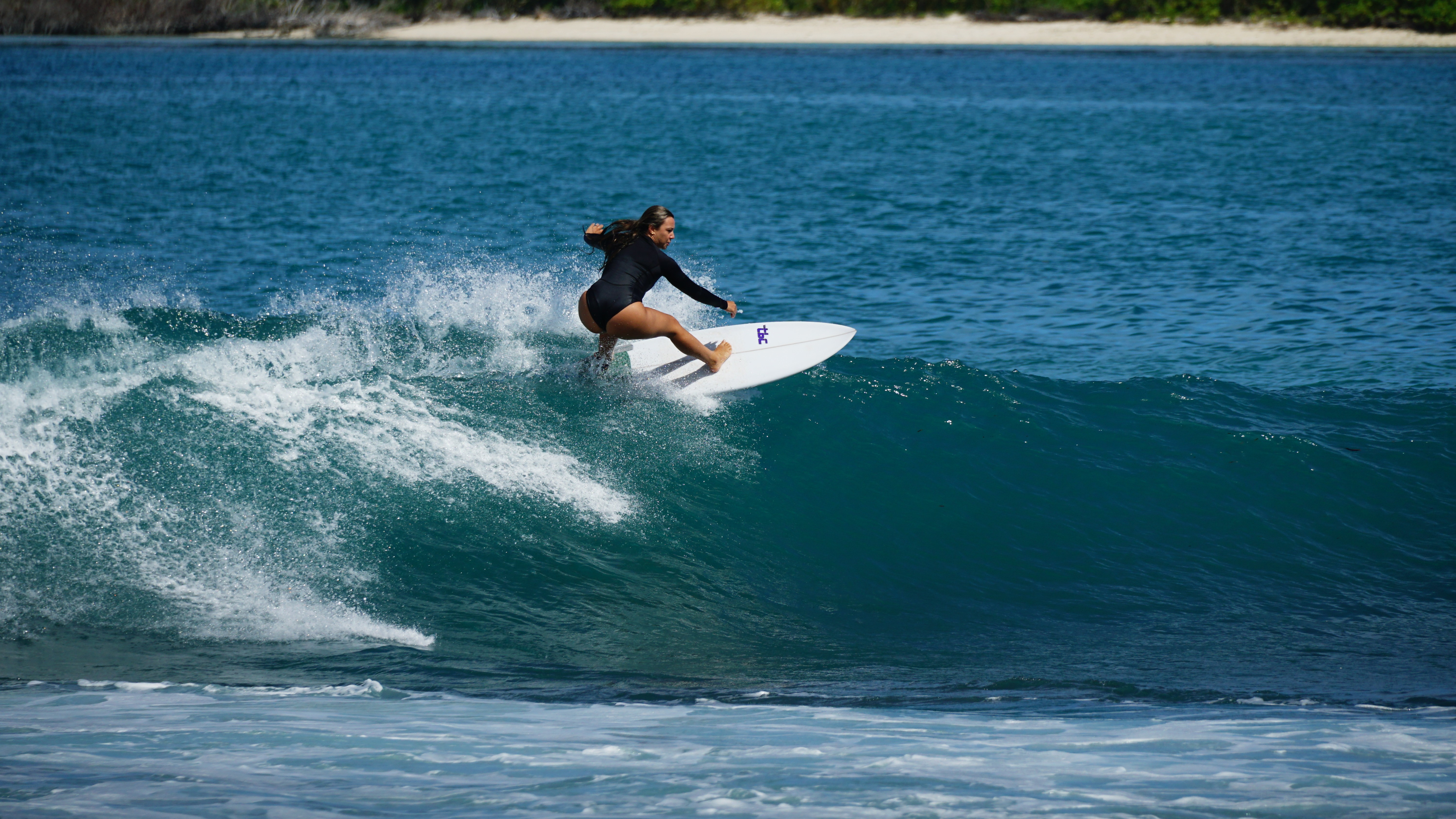 Person surfing on a wave in the ocean with a distant shoreline in the background.