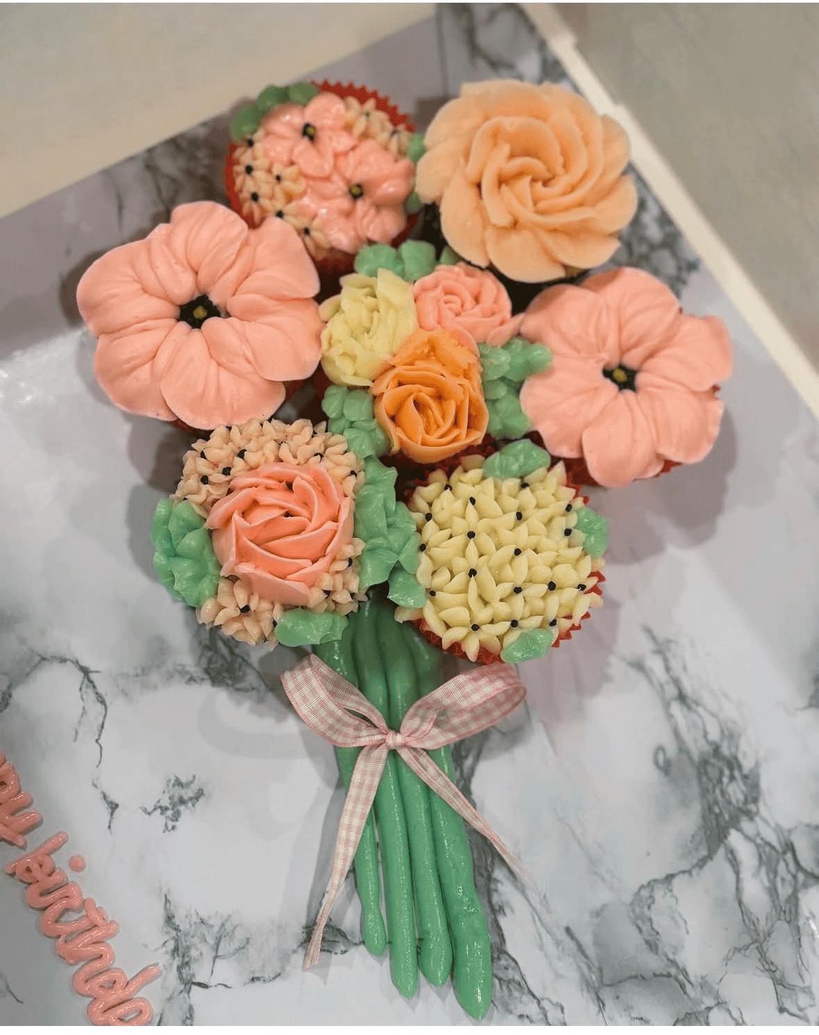 Bouquet of pastel-colored flowers with green stems, tied with a pink checkered ribbon, on a marble surface.