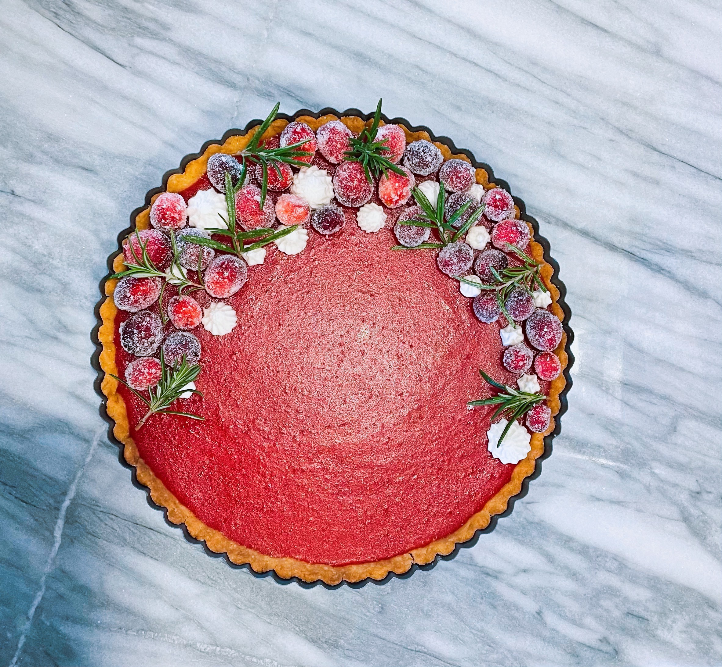 Round cake with pink frosting, decorated with berries and green leaves, on a marble surface.