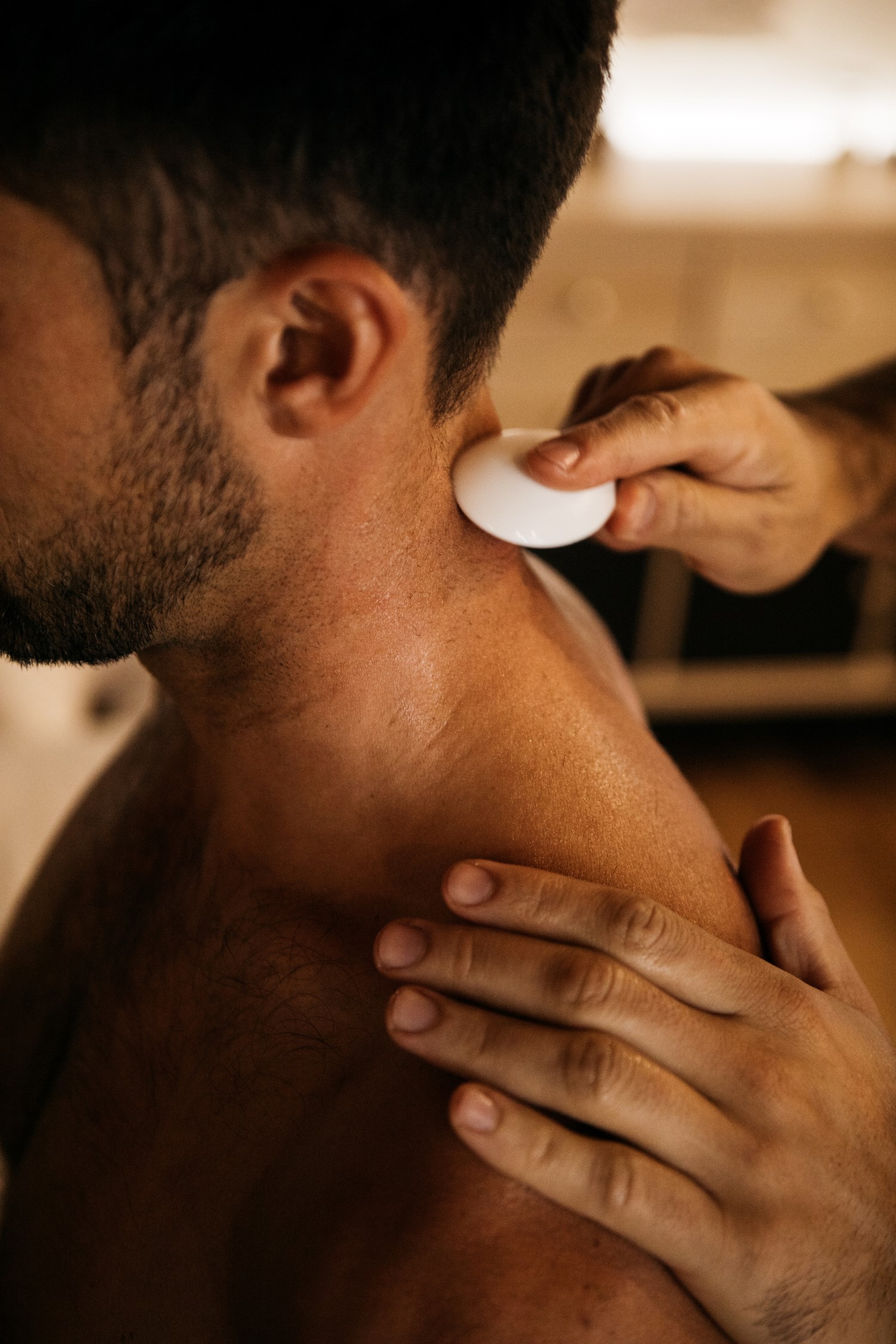 Person receiving a massage or therapy on neck with a white device, hands applying pressure, indoor setting.