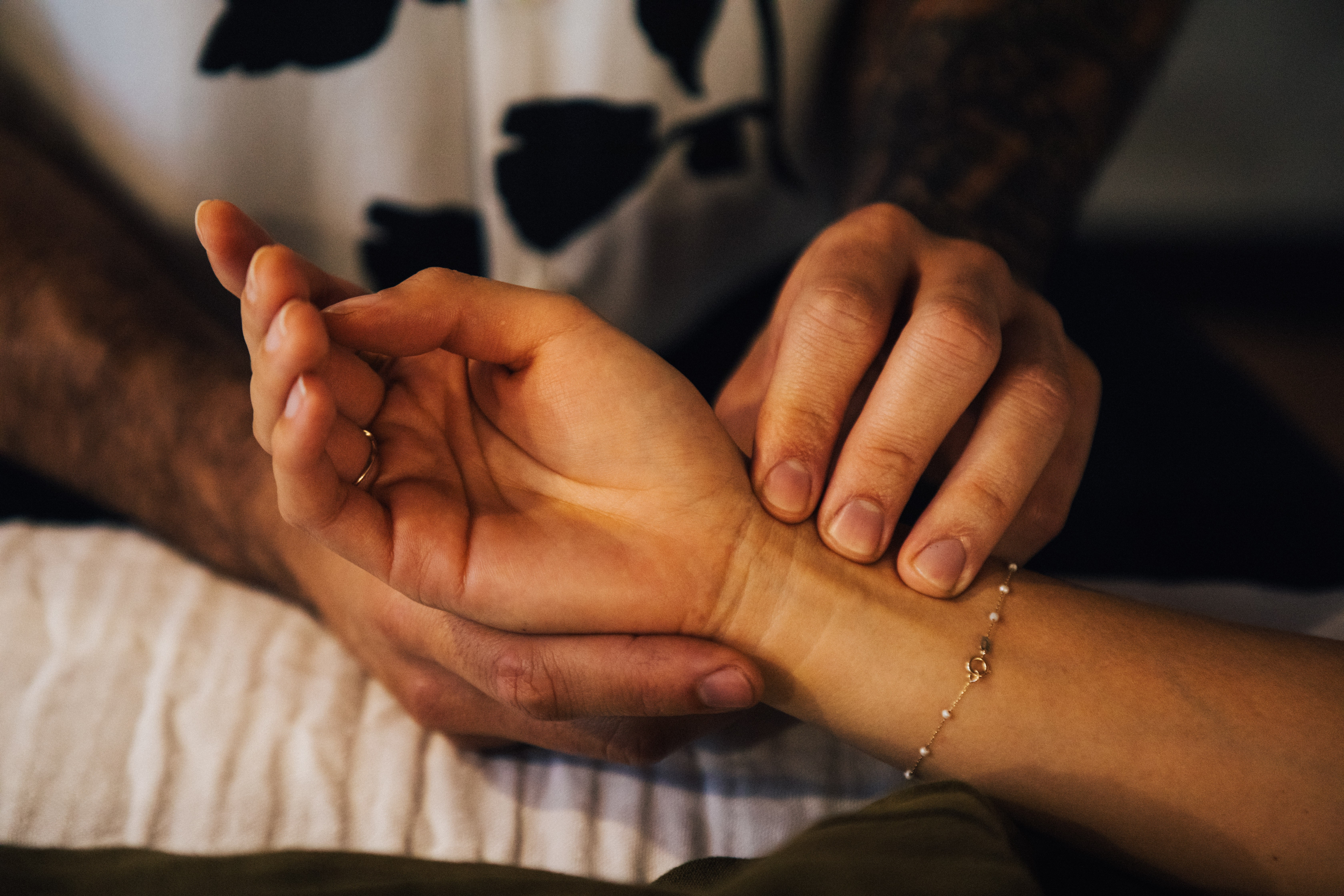 Two people hold hands, one with a bracelet, in a close-up shot, with a blurred background.