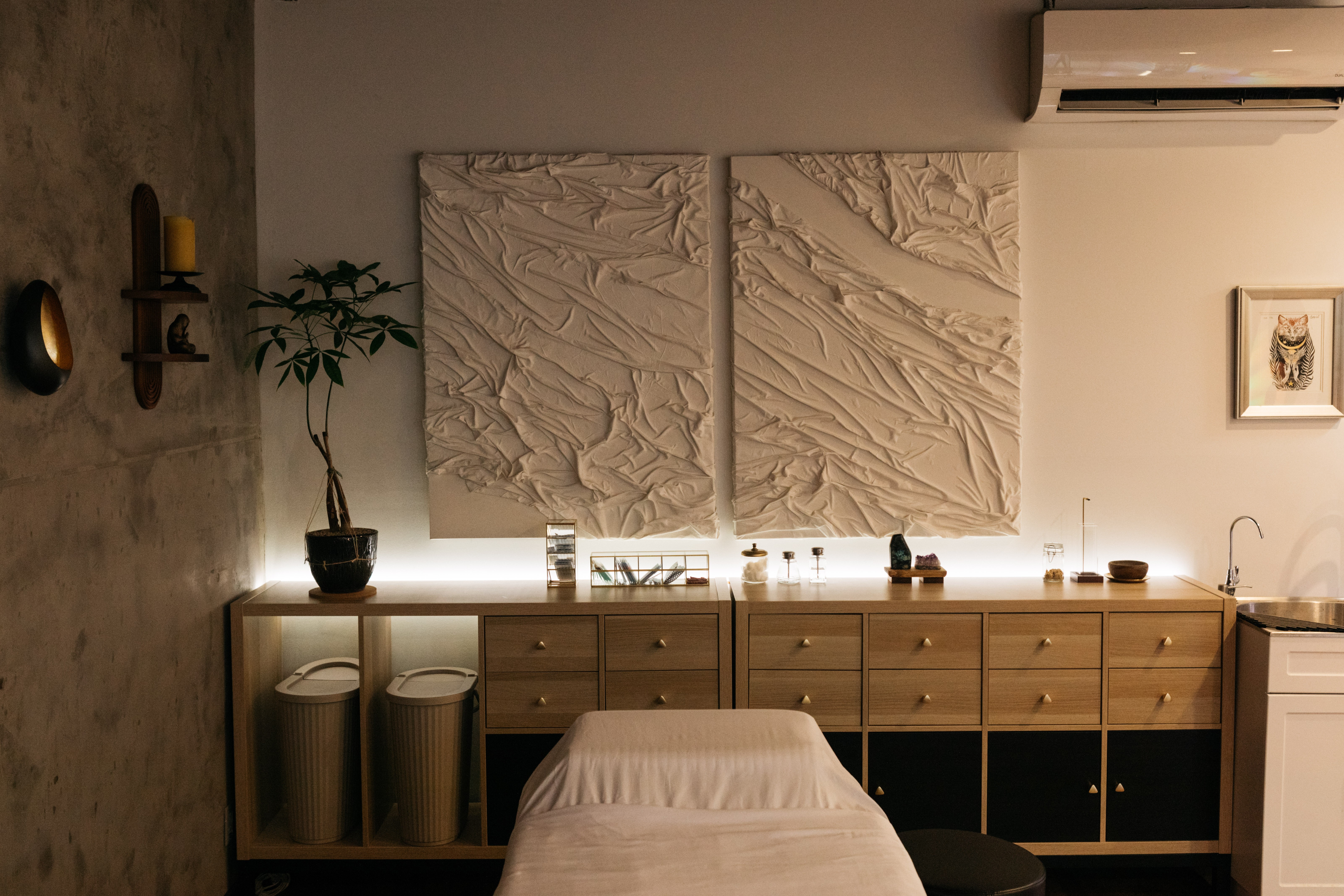 Upright view of a room with a bed, artwork, and decorative items on the wall, with a sideboard and plants.