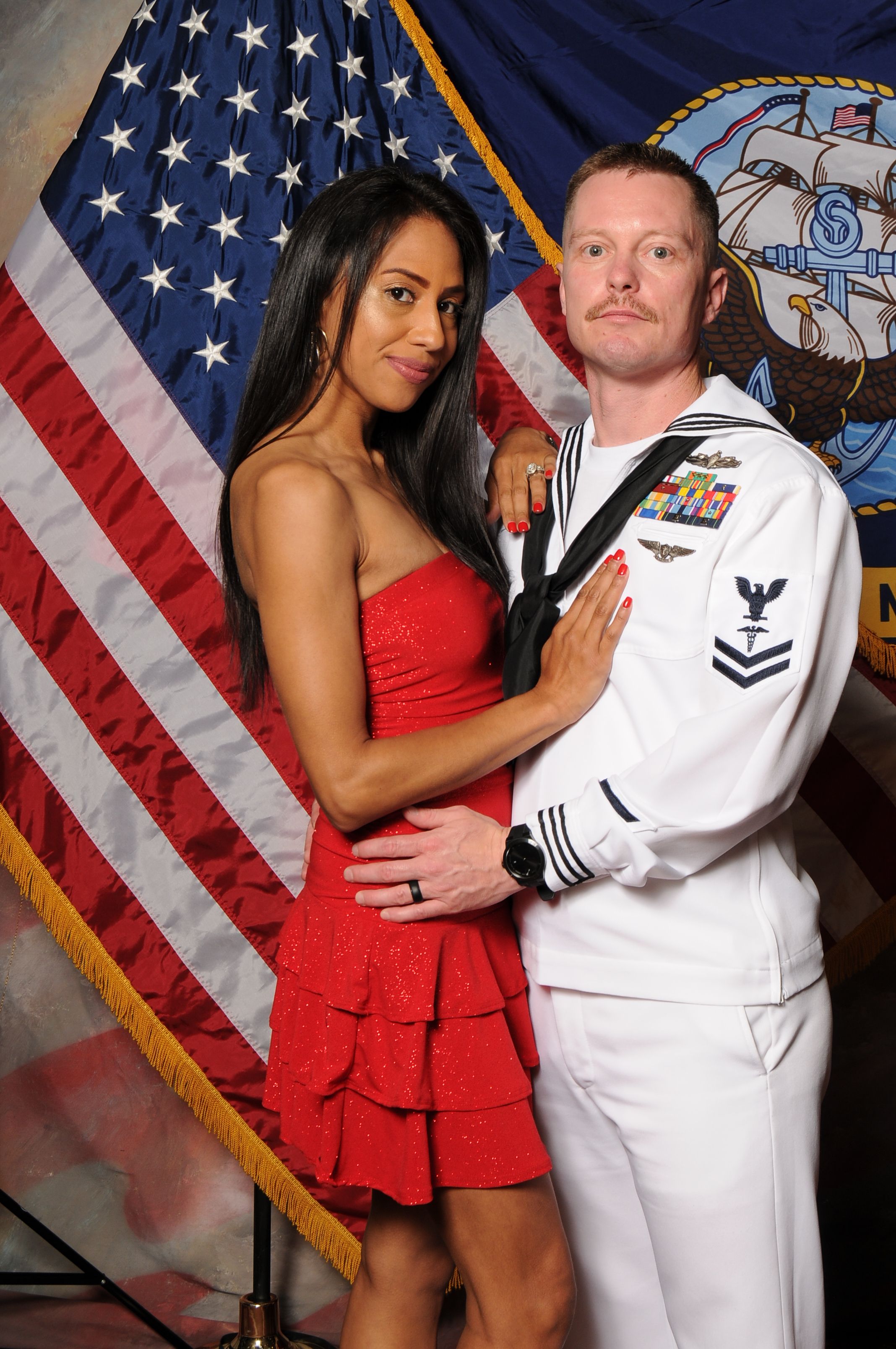 A woman in a red dress lying on an American flag, with a man in a military uniform beside her, indoors.