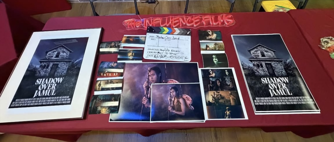 Table with books, photographs, and a check, with a red sign reading 'INFLUENCE FILMS' in the background.