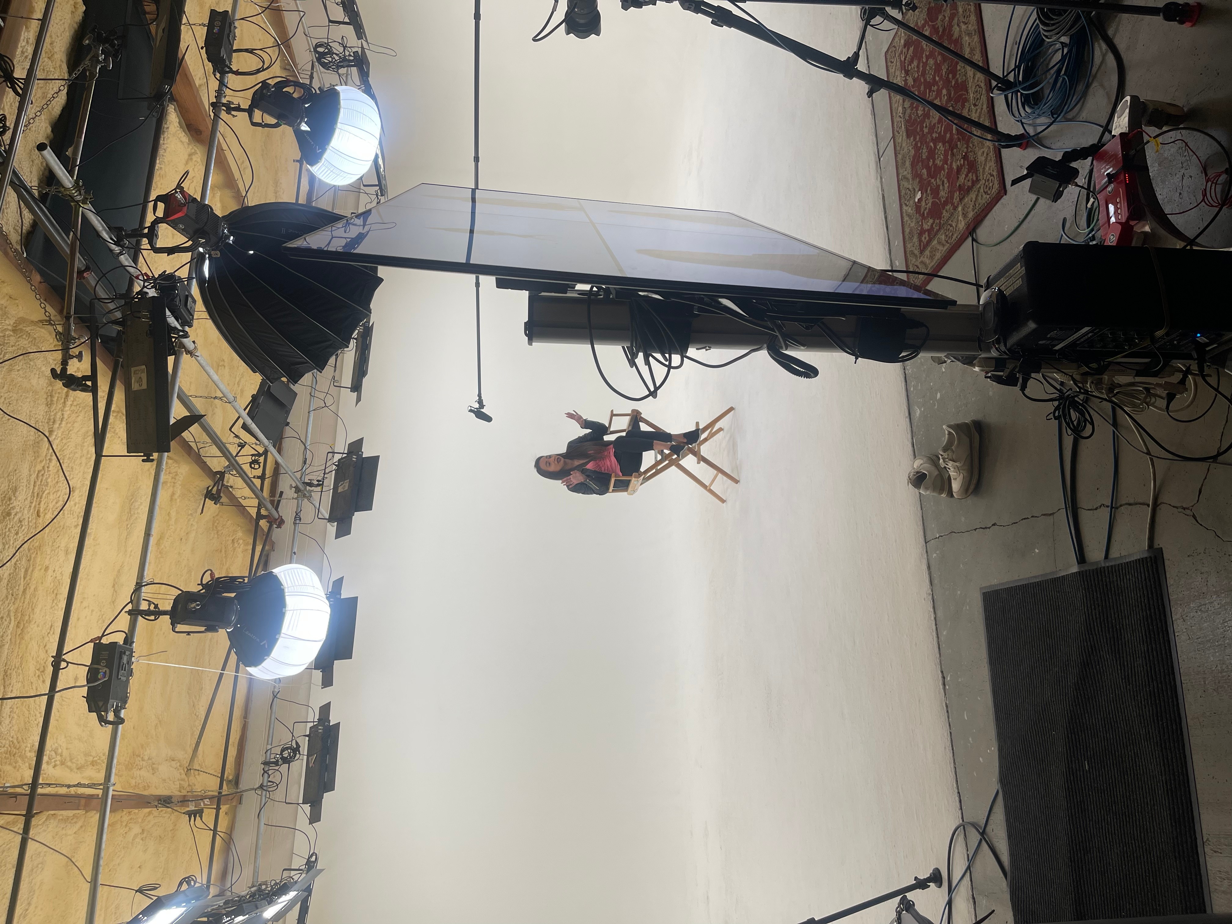 Studio with a person hanging from a harness, surrounded by lighting and equipment, and a white backdrop.