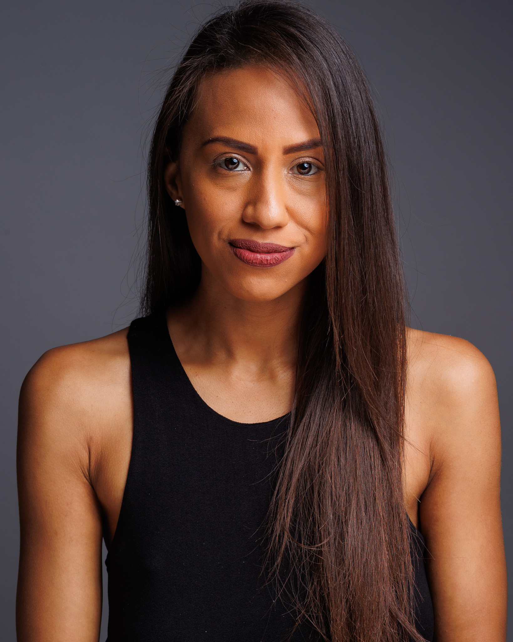 A woman with long straight hair wearing a black sleeveless top, looking at the camera with a slight smile.