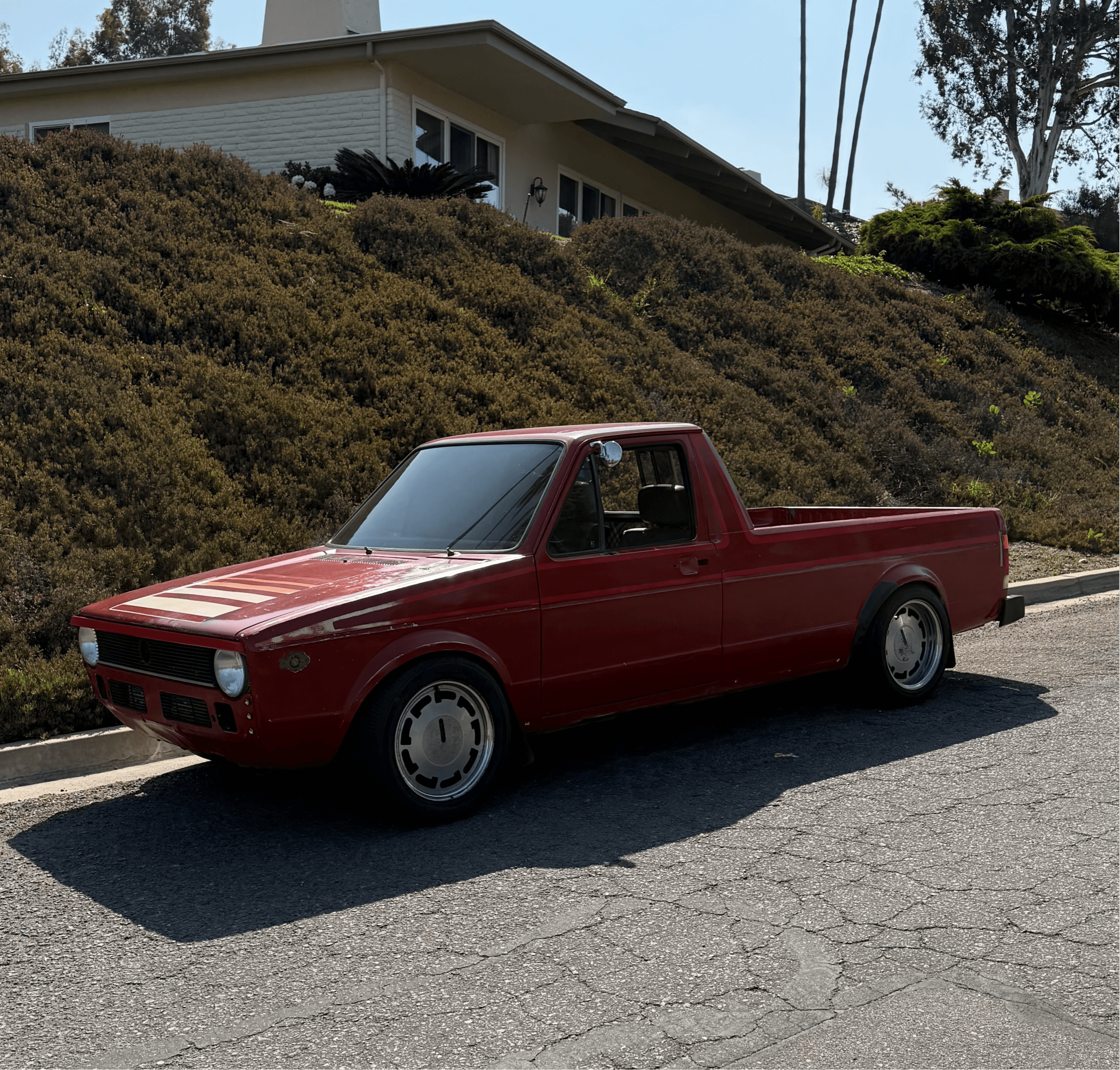 Red pickup truck parked on street with hillside and house in background.