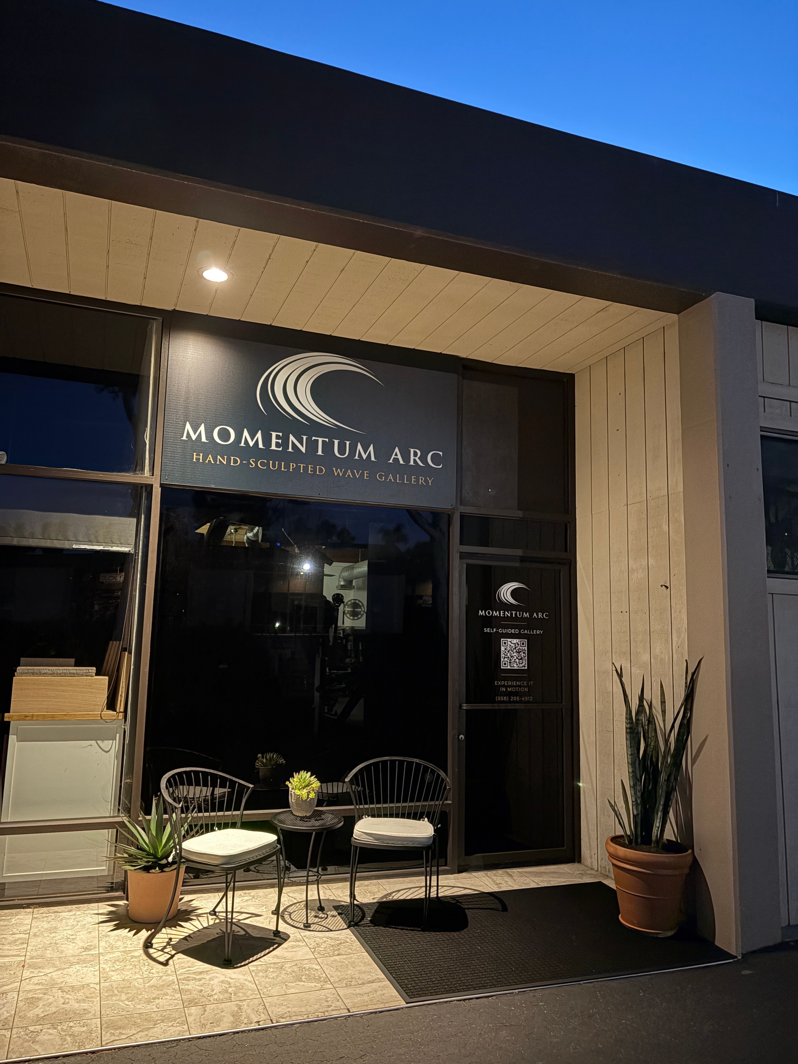Storefront with a sign reading 'Momentum ARC,' glass door, potted plants, and outdoor seating area.