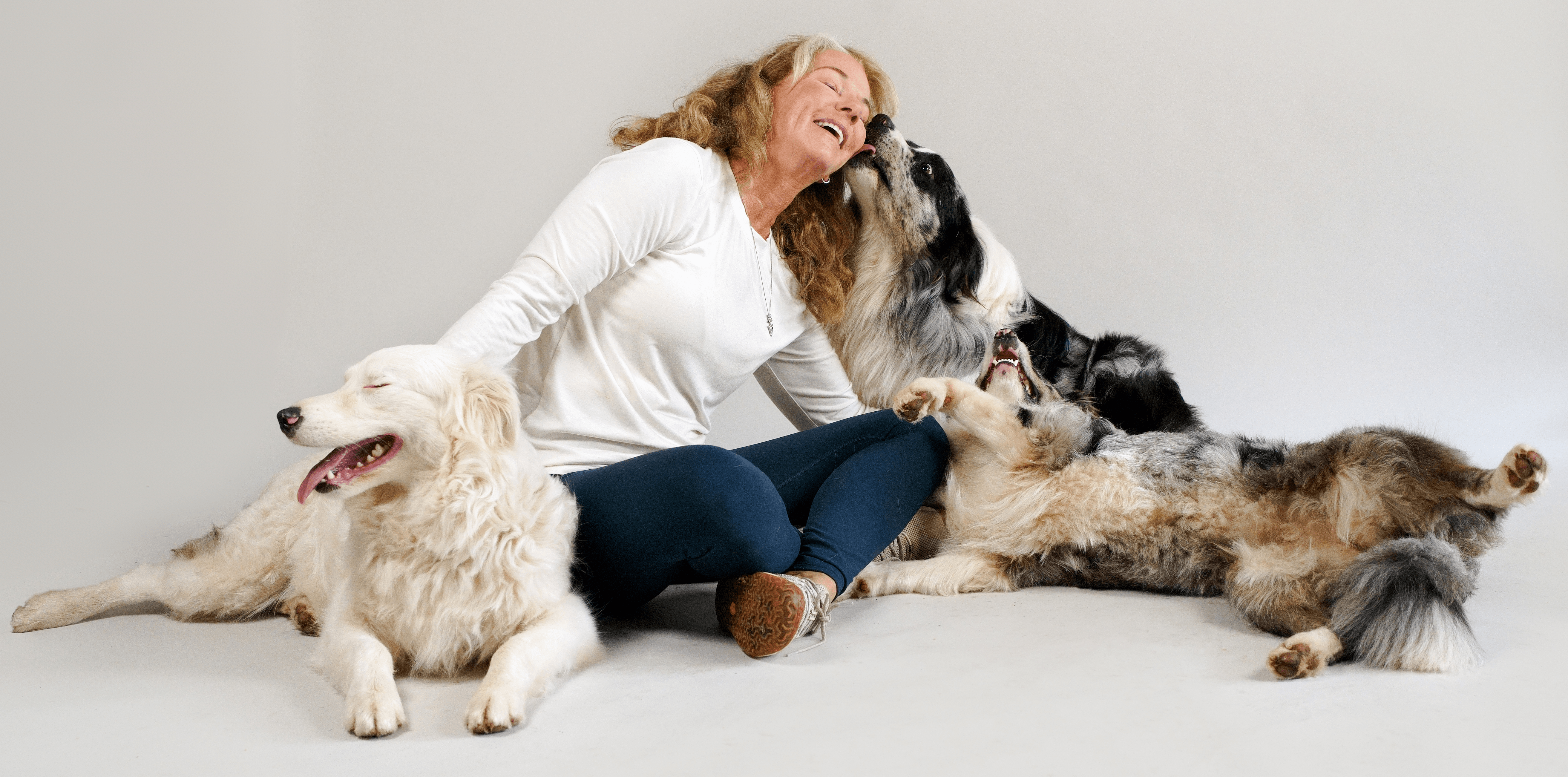 Woman laughing with five dogs lying around her on a plain white background.