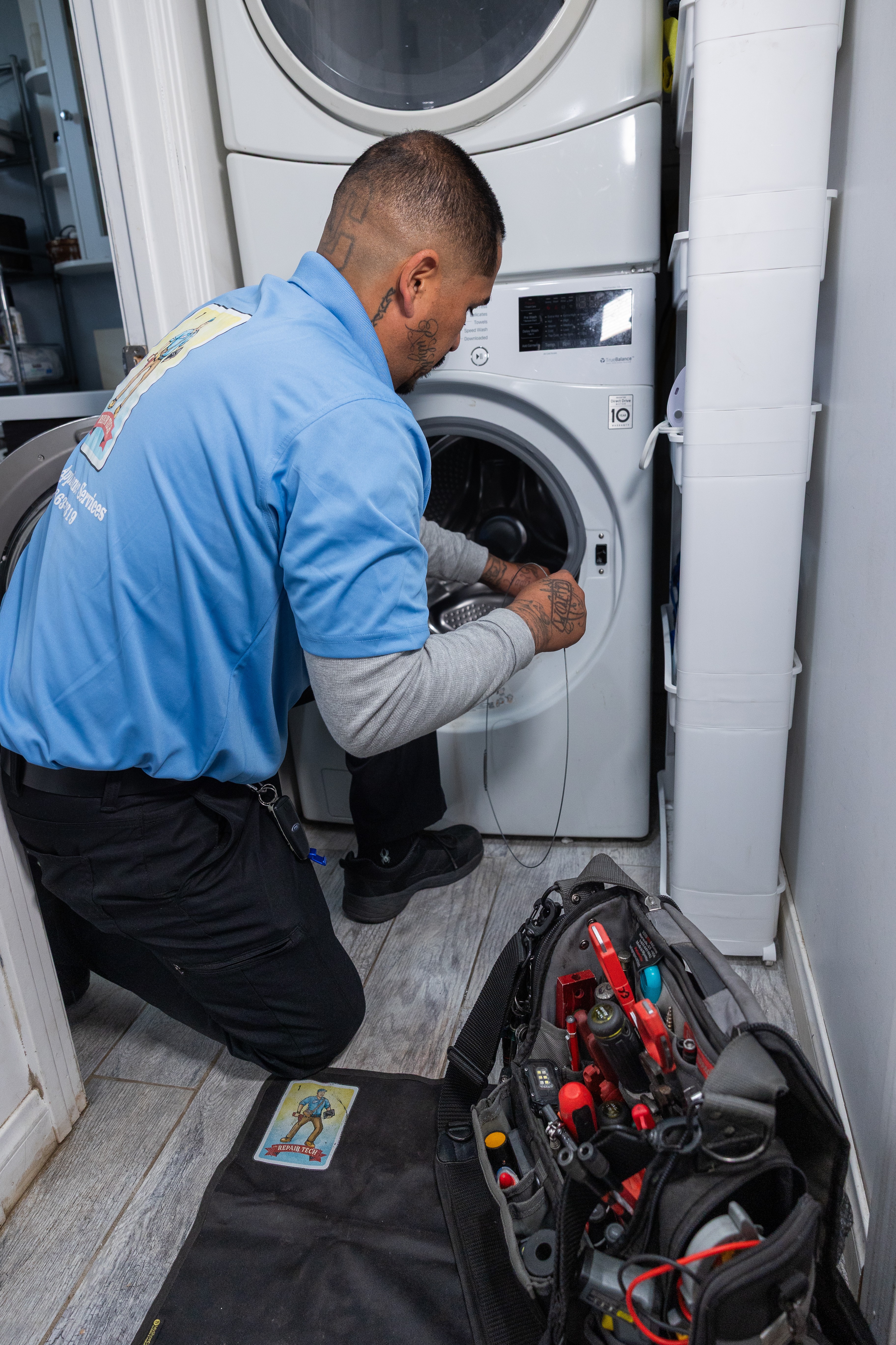 Technician repairing washing machine in laundry room with tools and equipment nearby.