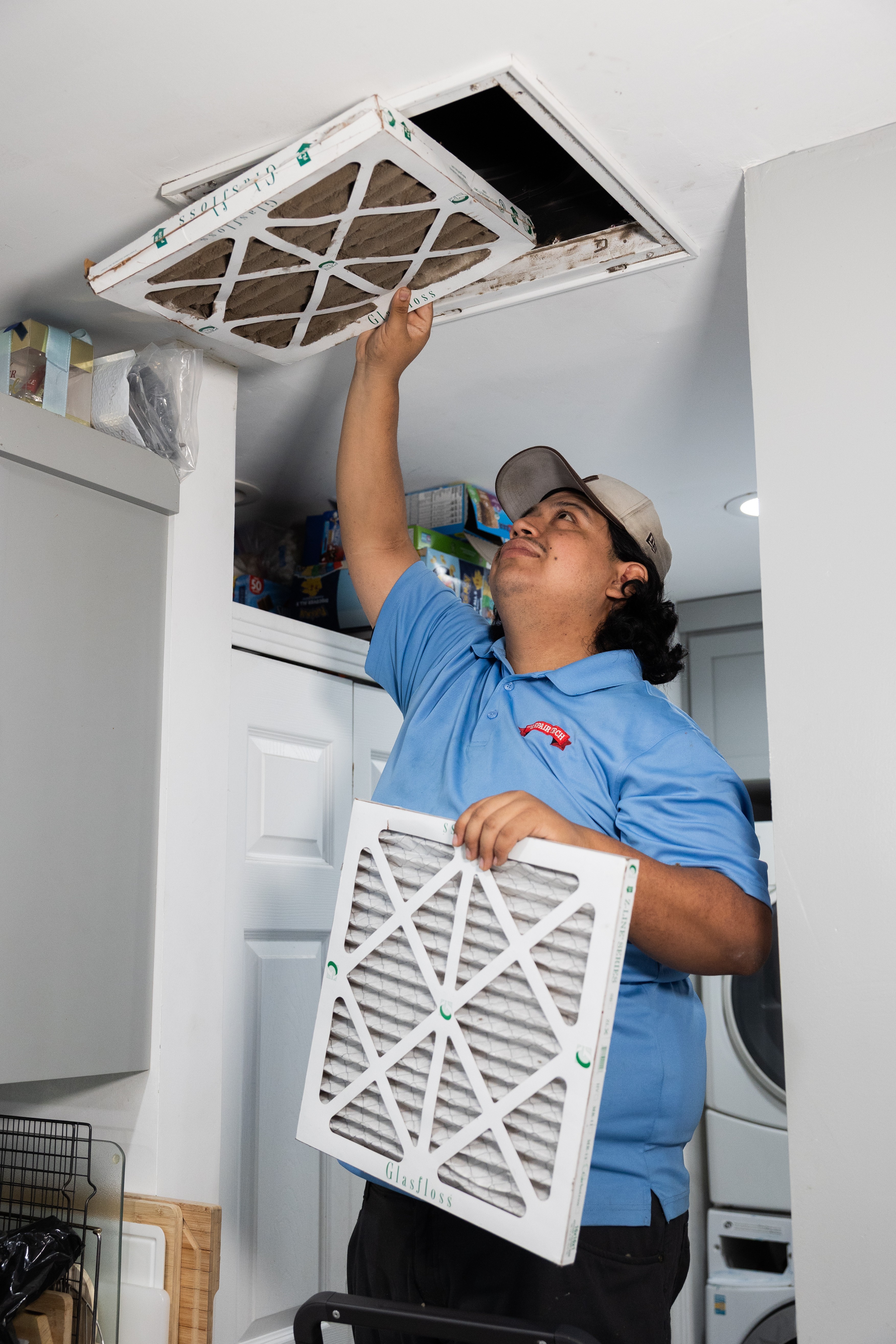 Technician installing or repairing an air conditioning unit in a ceiling, holding a filter, in a laundry room.