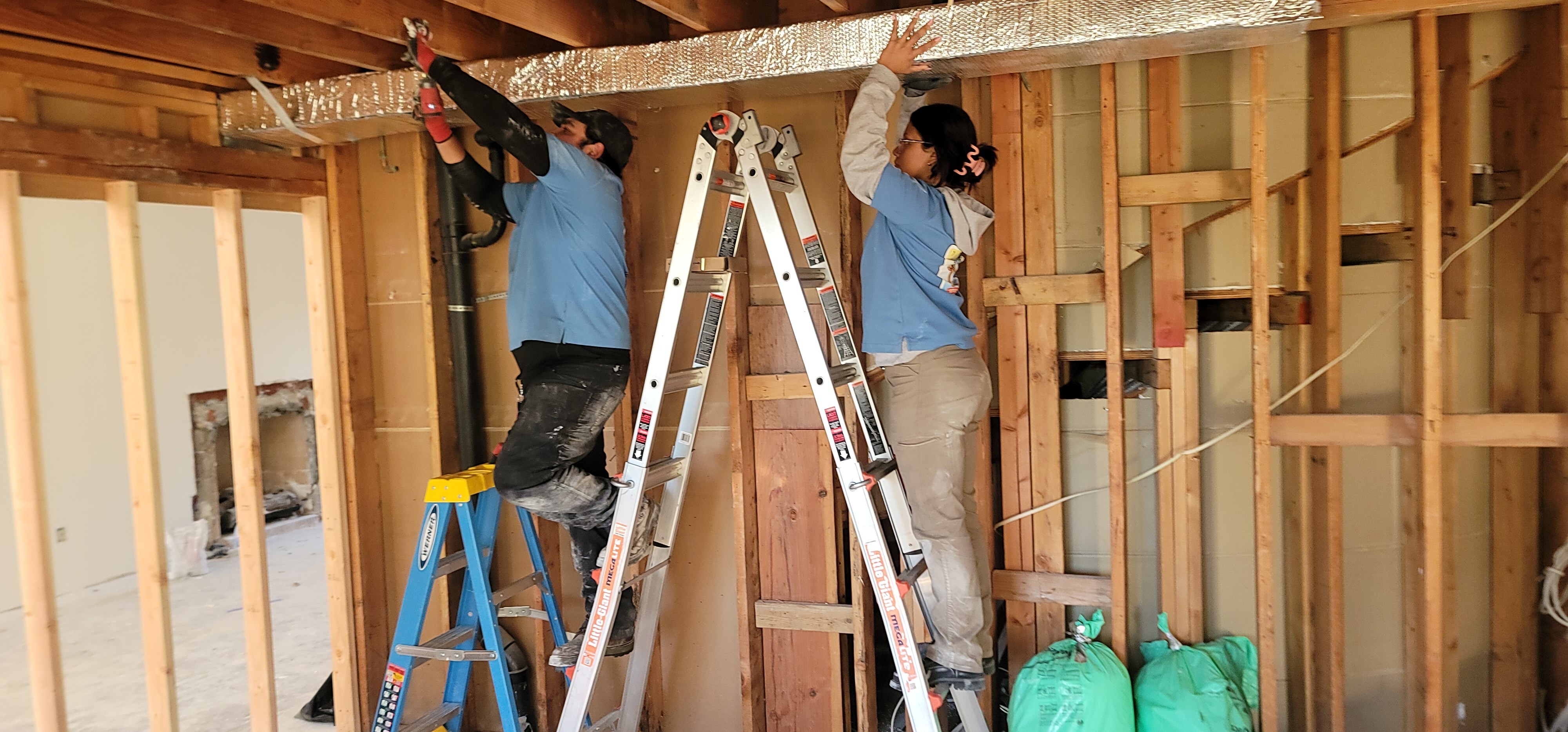 Two workers on ladders installing wooden beams in a building under construction.