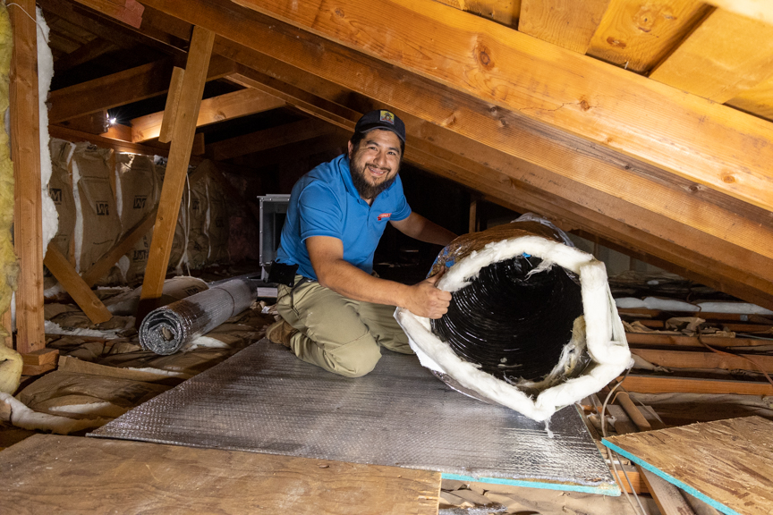 Person kneeling on a mat in an attic, holding a large black and white object, with wooden beams overhead.