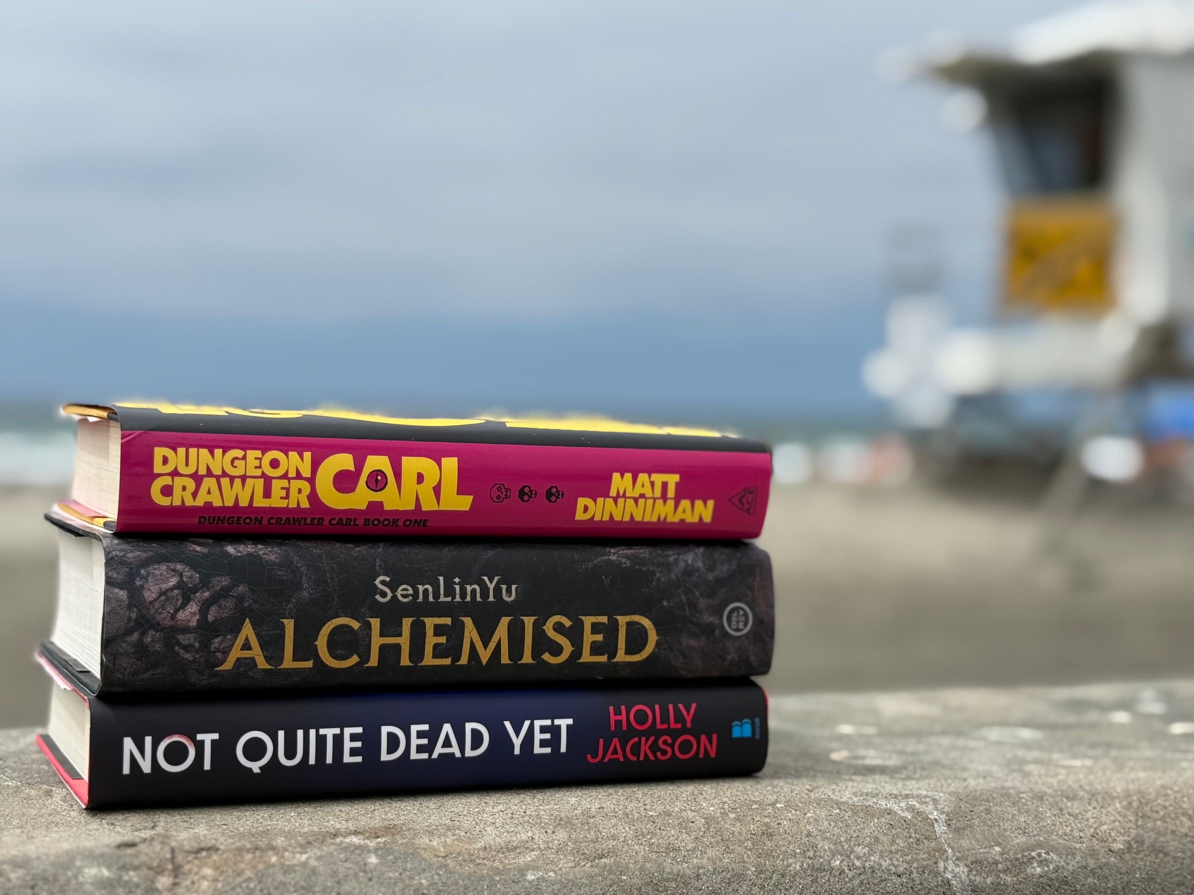 Three books stacked on a surface outdoors with a blurred boat and sky in the background.