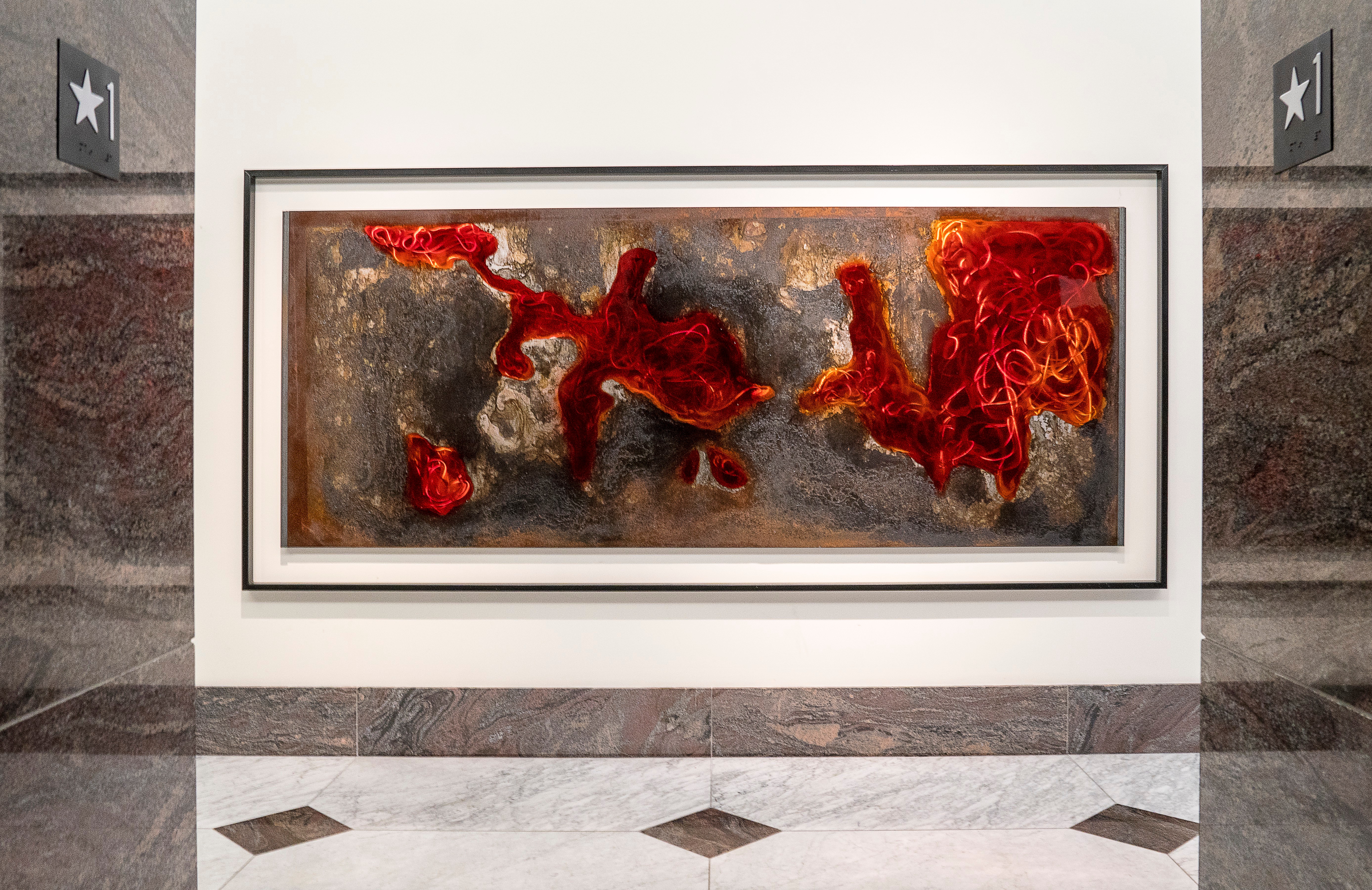 Abstract artwork with red, orange, and black colors in a rectangular frame on a white wall, with marble floors and directional signs.