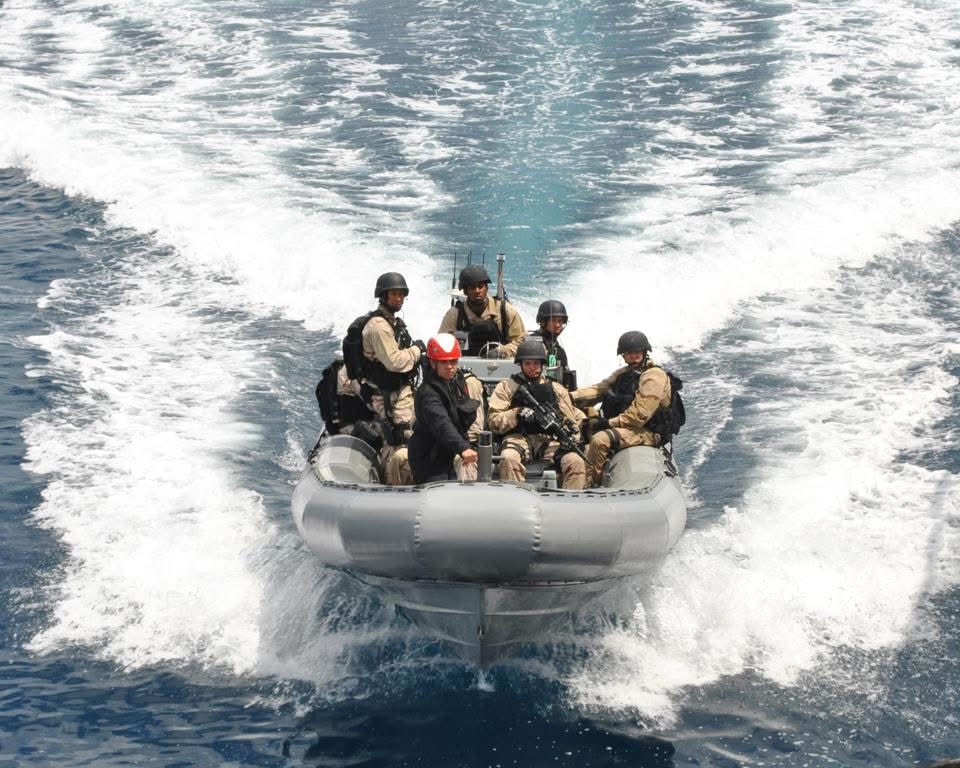 Group of people in a boat on water, wearing helmets and life jackets, moving quickly through the water.