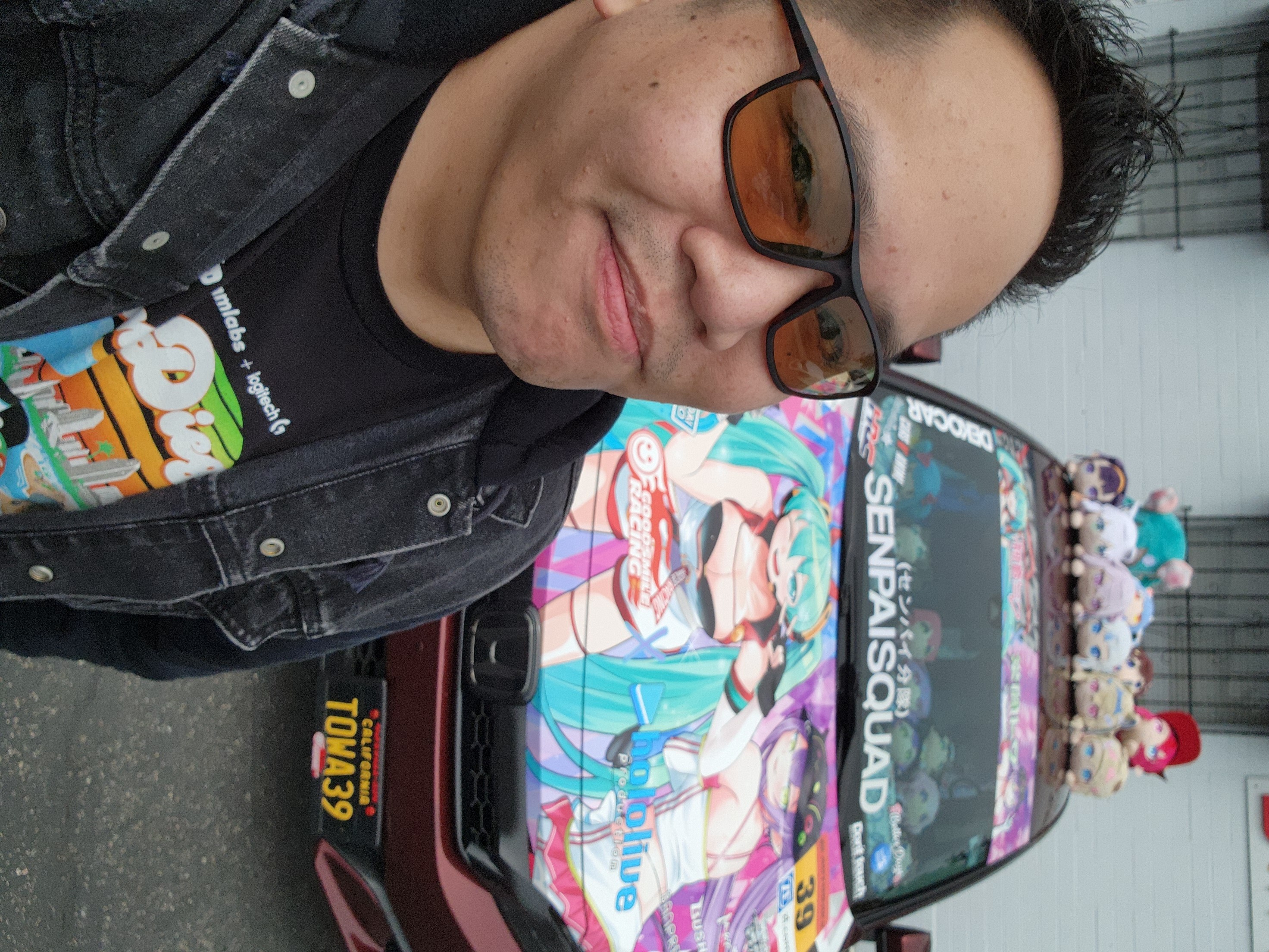 Person wearing sunglasses and a black jacket standing next to a decorated vehicle with colorful artwork and text.