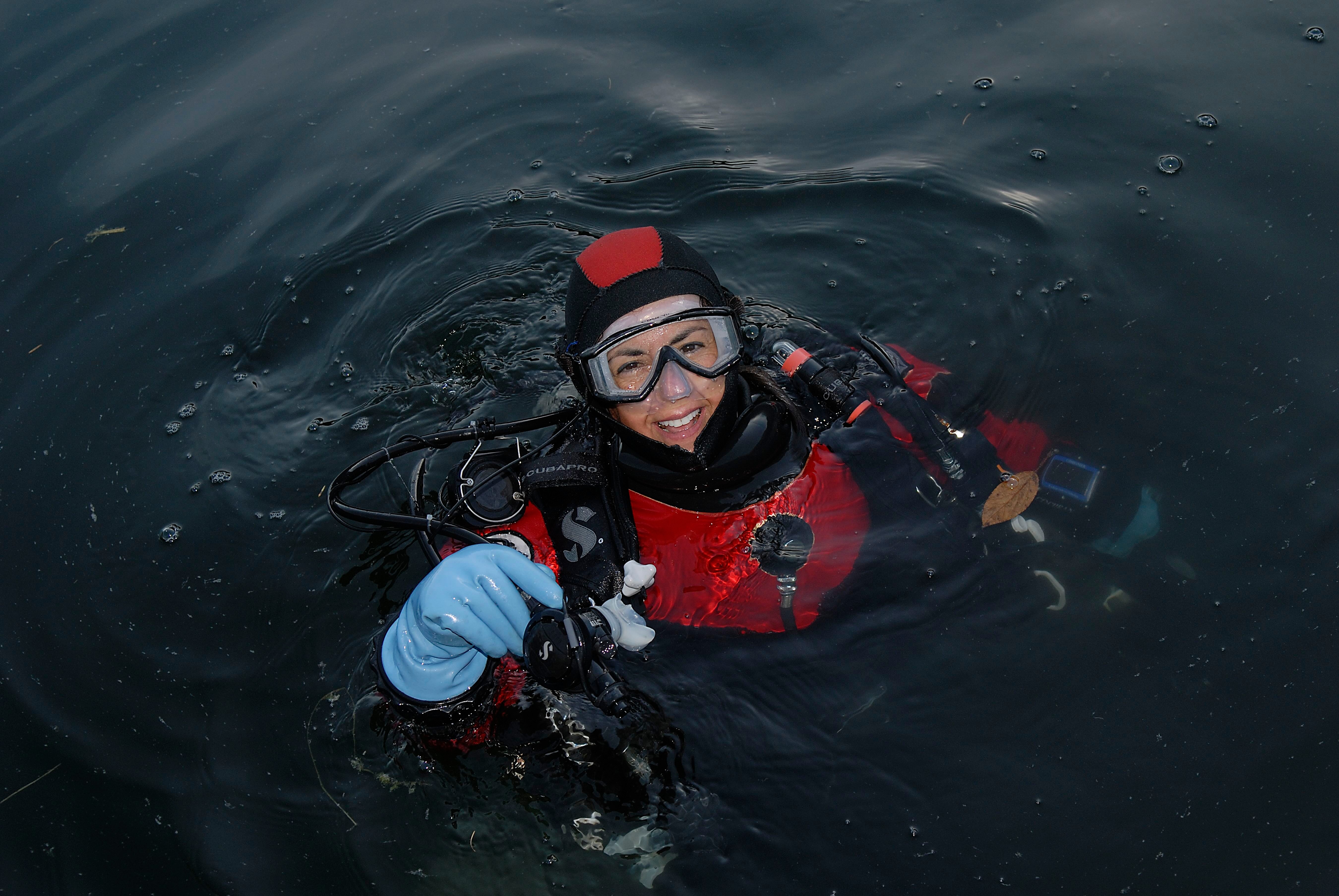 Person in diving gear floating in water, smiling, wearing a red and black wetsuit, mask, and gloves.