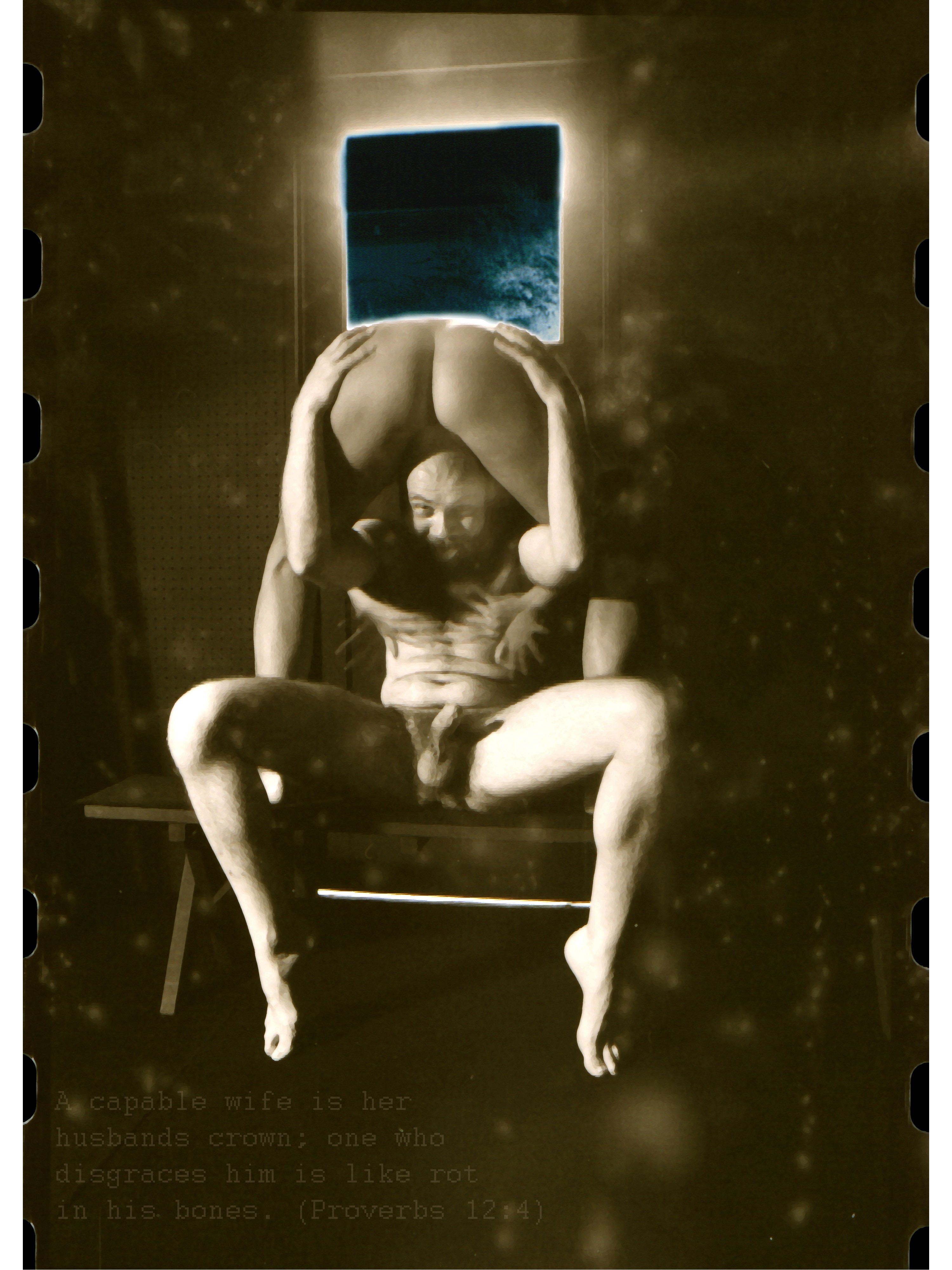 Person sitting on a chair with legs spread, holding a mirror above their head, reflecting a window or light source, in a dim room.